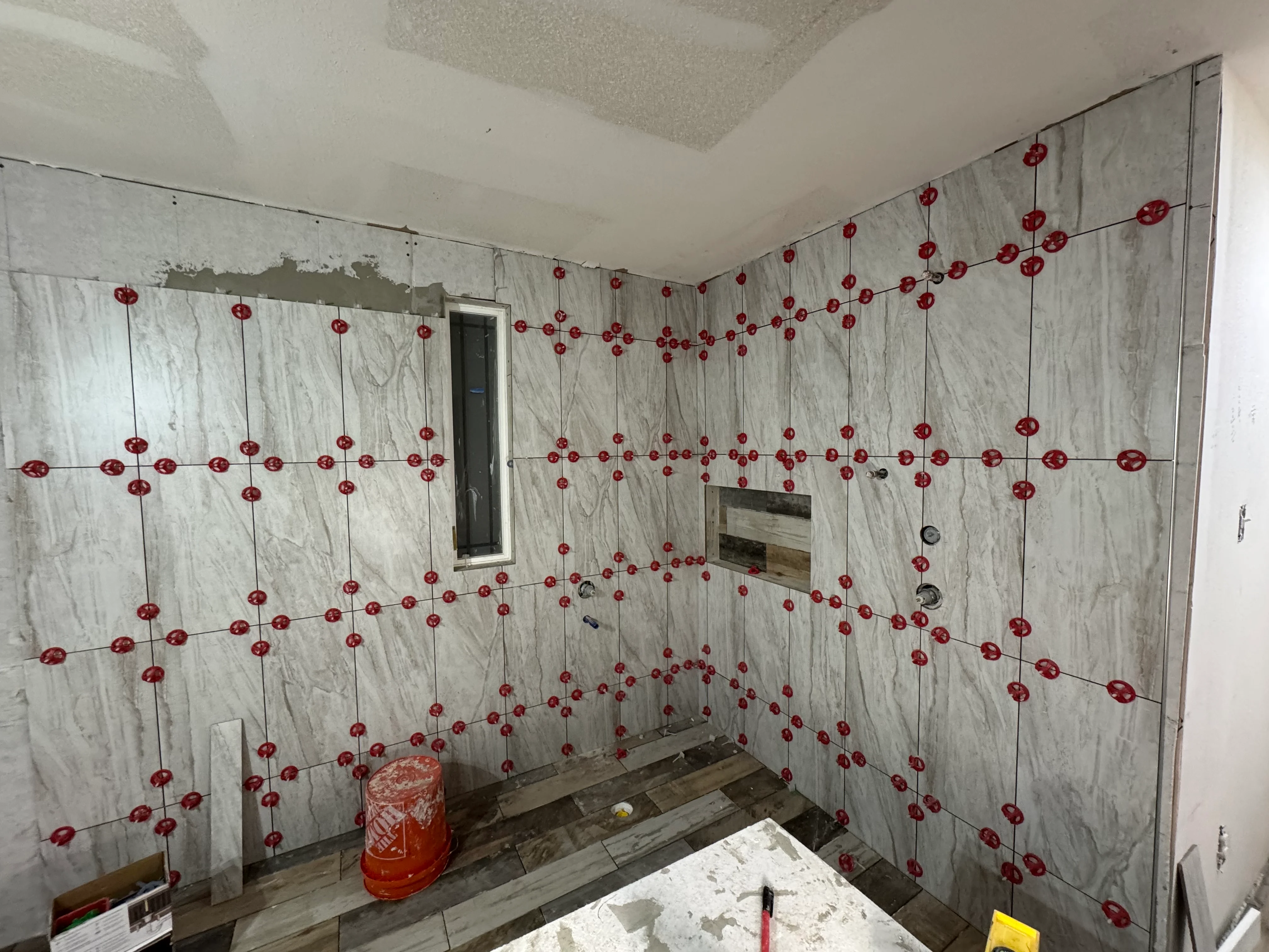 Bathroom under remodel with marble tile walls and red decorative accents during installation phase