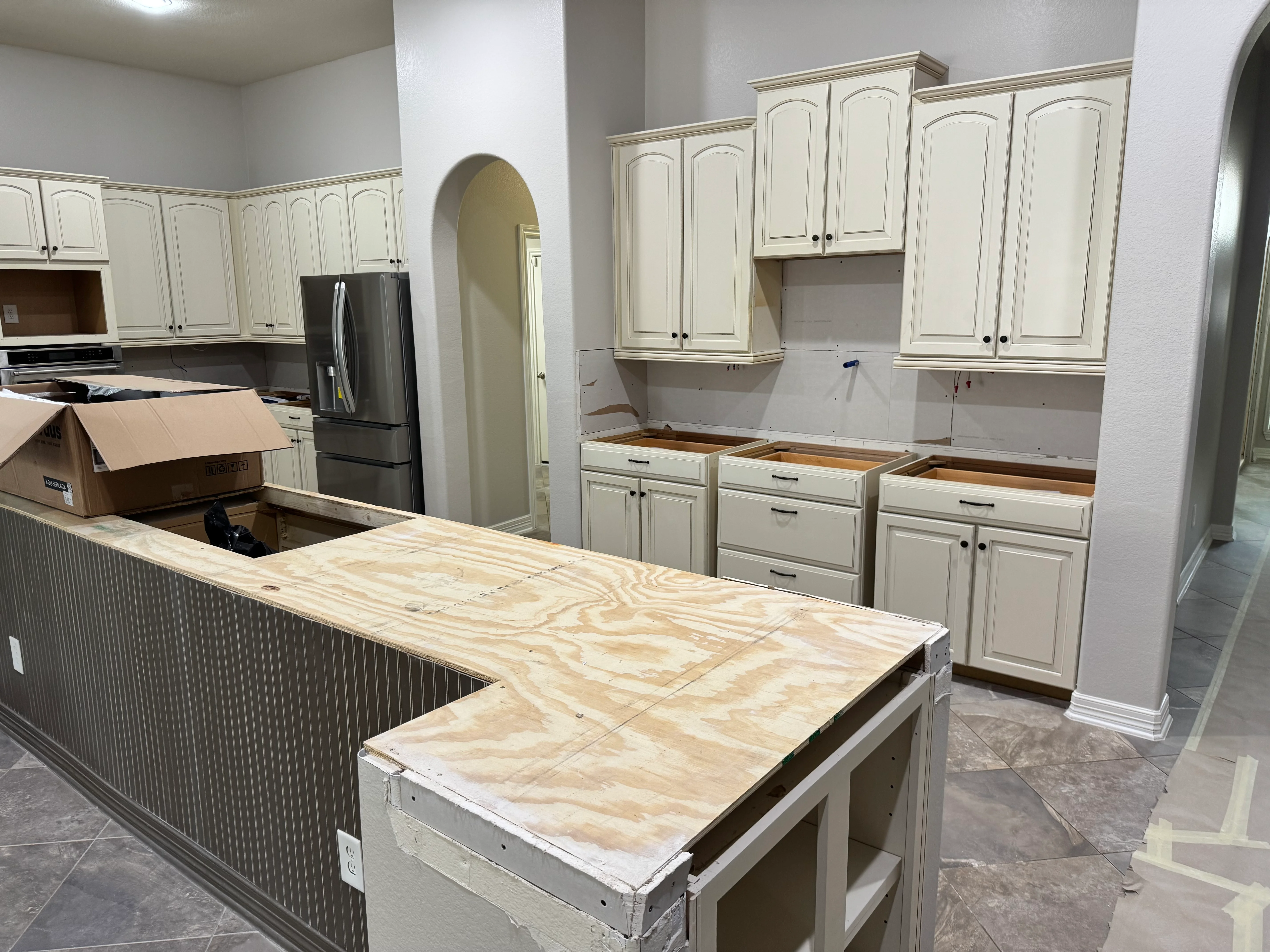 Kitchen remodel in progress with cream cabinetry and plywood countertop substrate