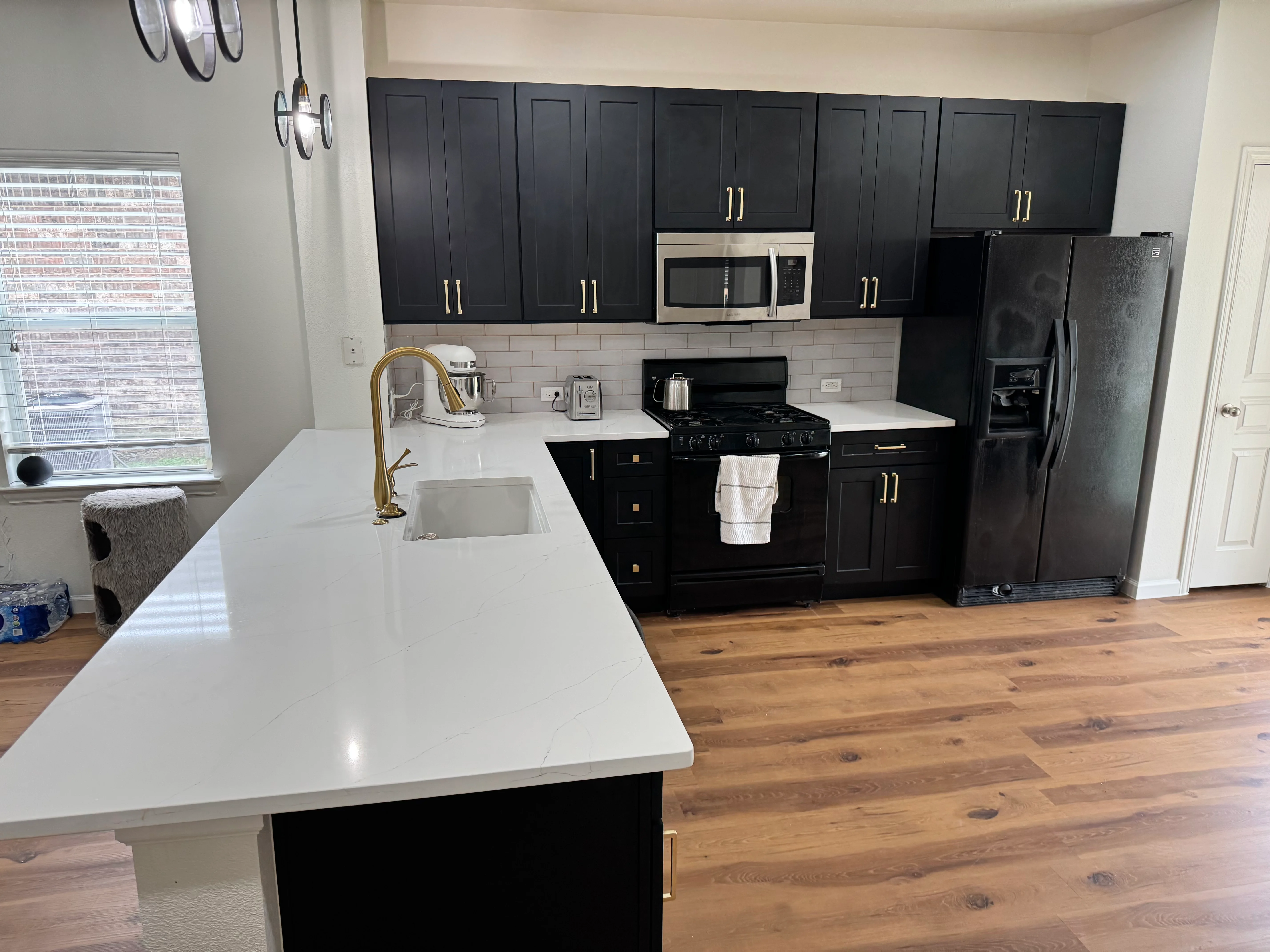 Modern kitchen with black cabinets, white quartz counters, and stainless steel appliances