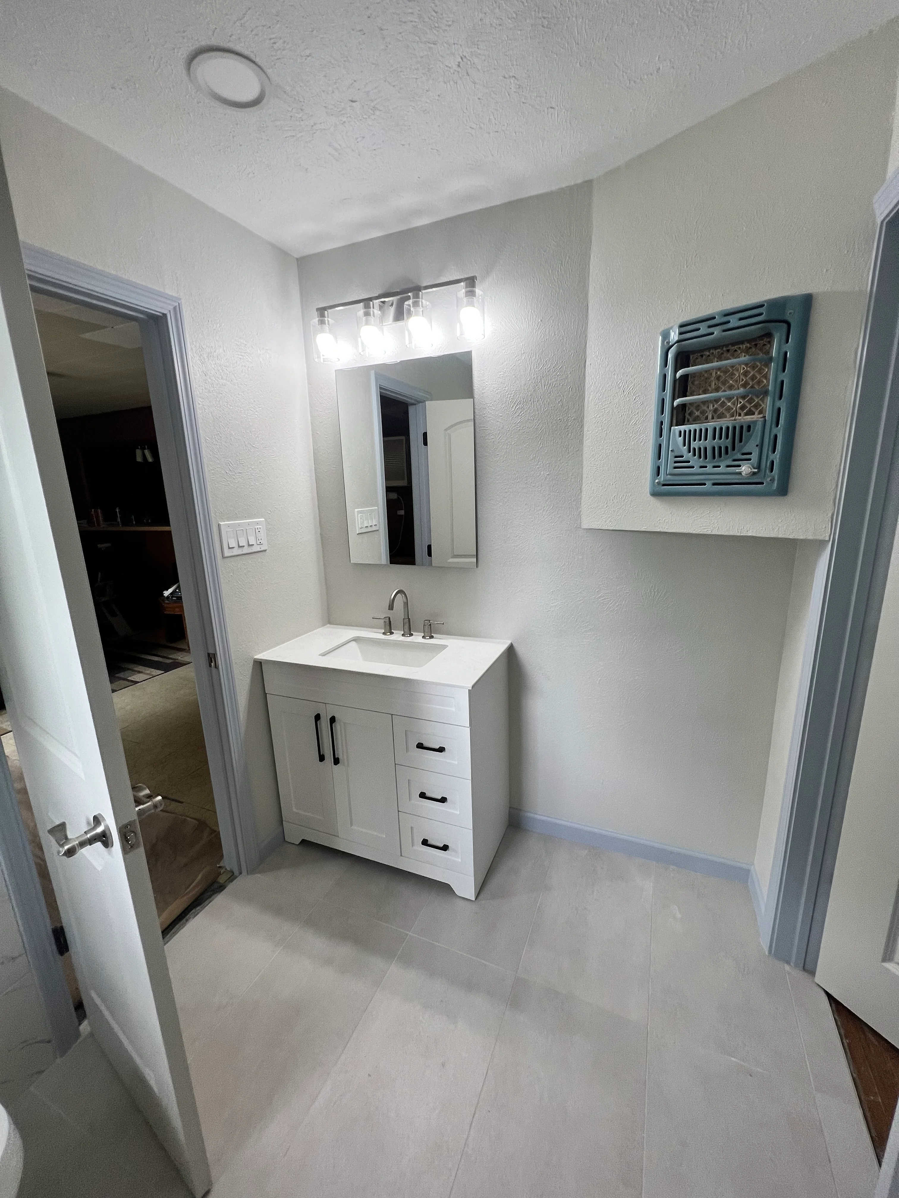 Newly remodeled bathroom with white vanity, mirror, and light gray tile flooring