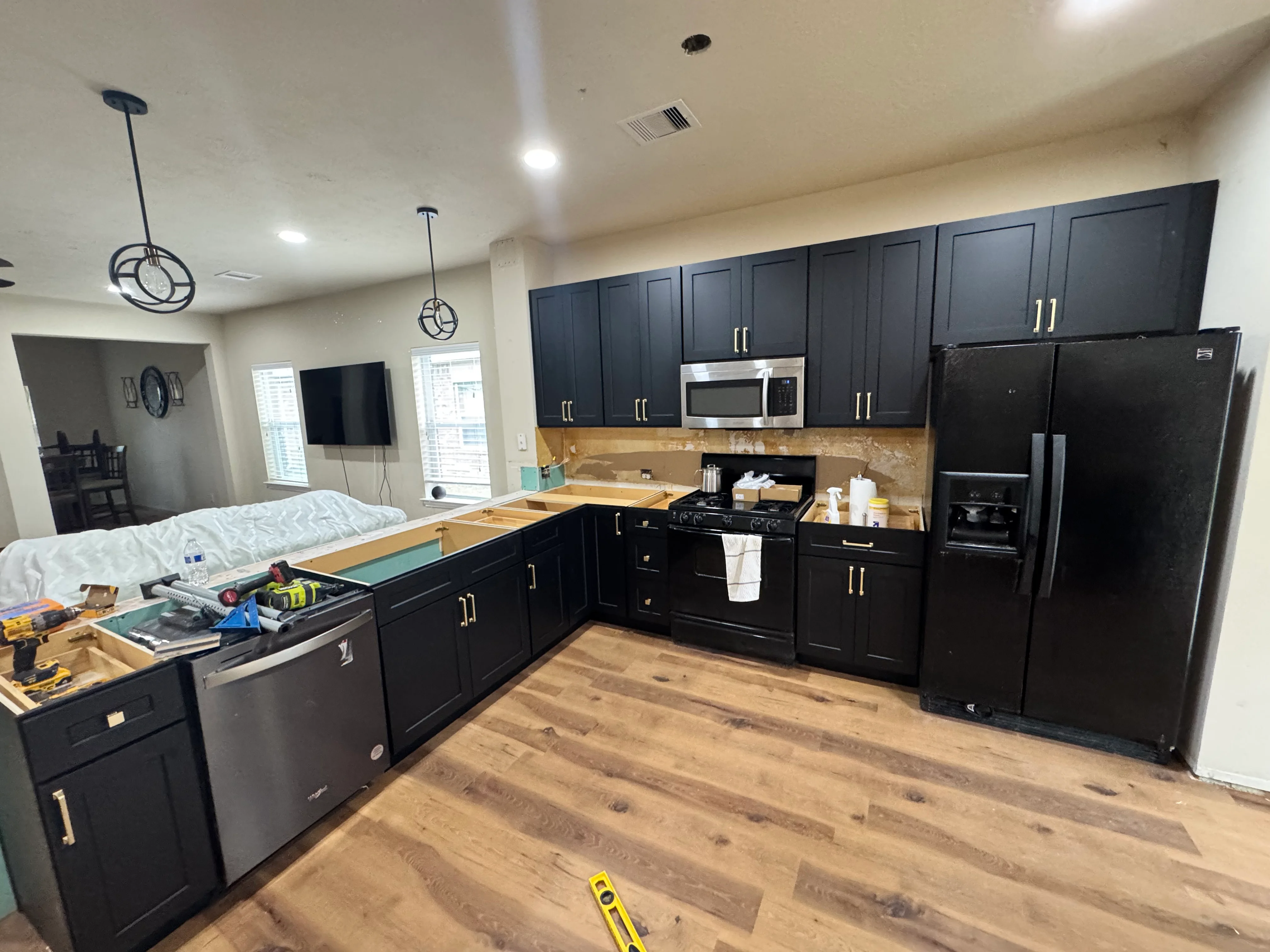 Modern kitchen with black cabinets, wood flooring, and stainless steel appliances during installation