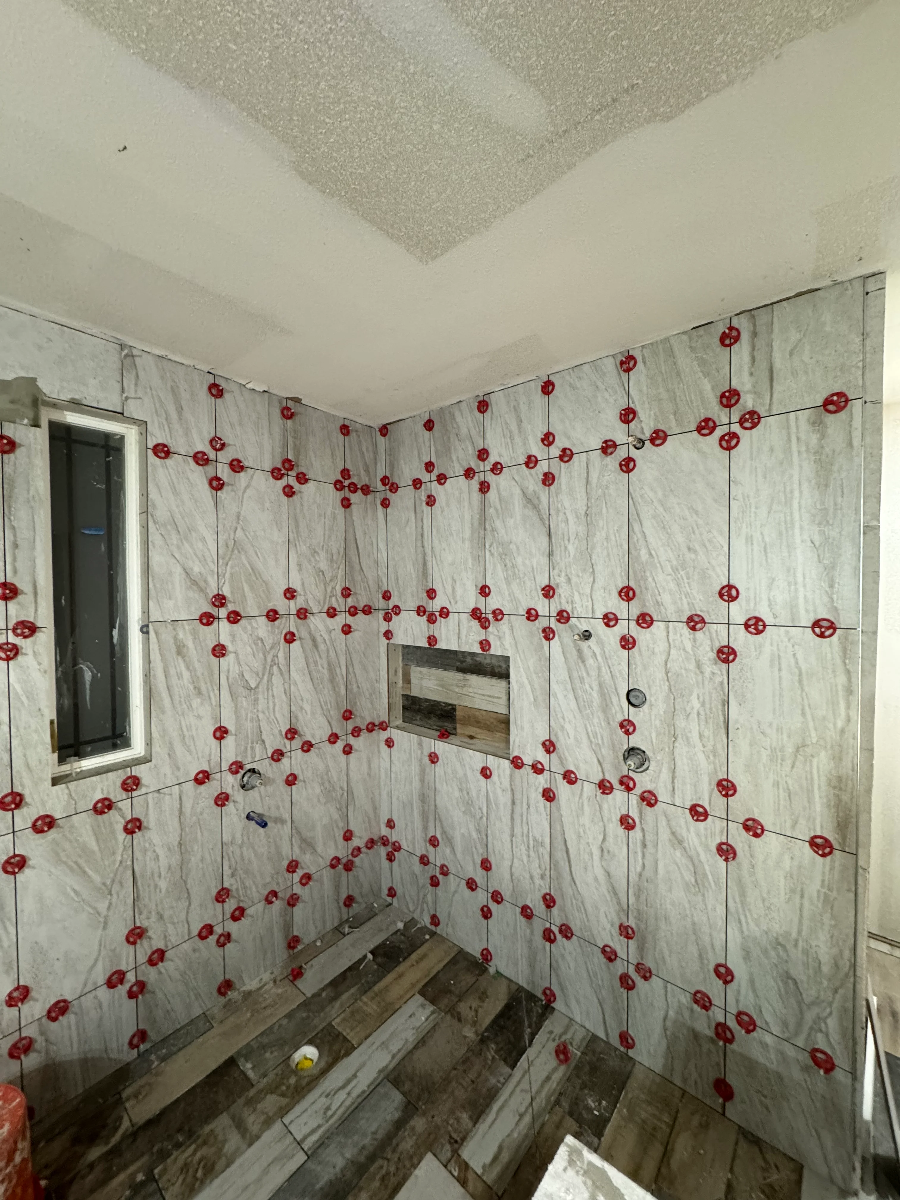 Bathroom shower walls with marble-look tile and red spacer dots during installation