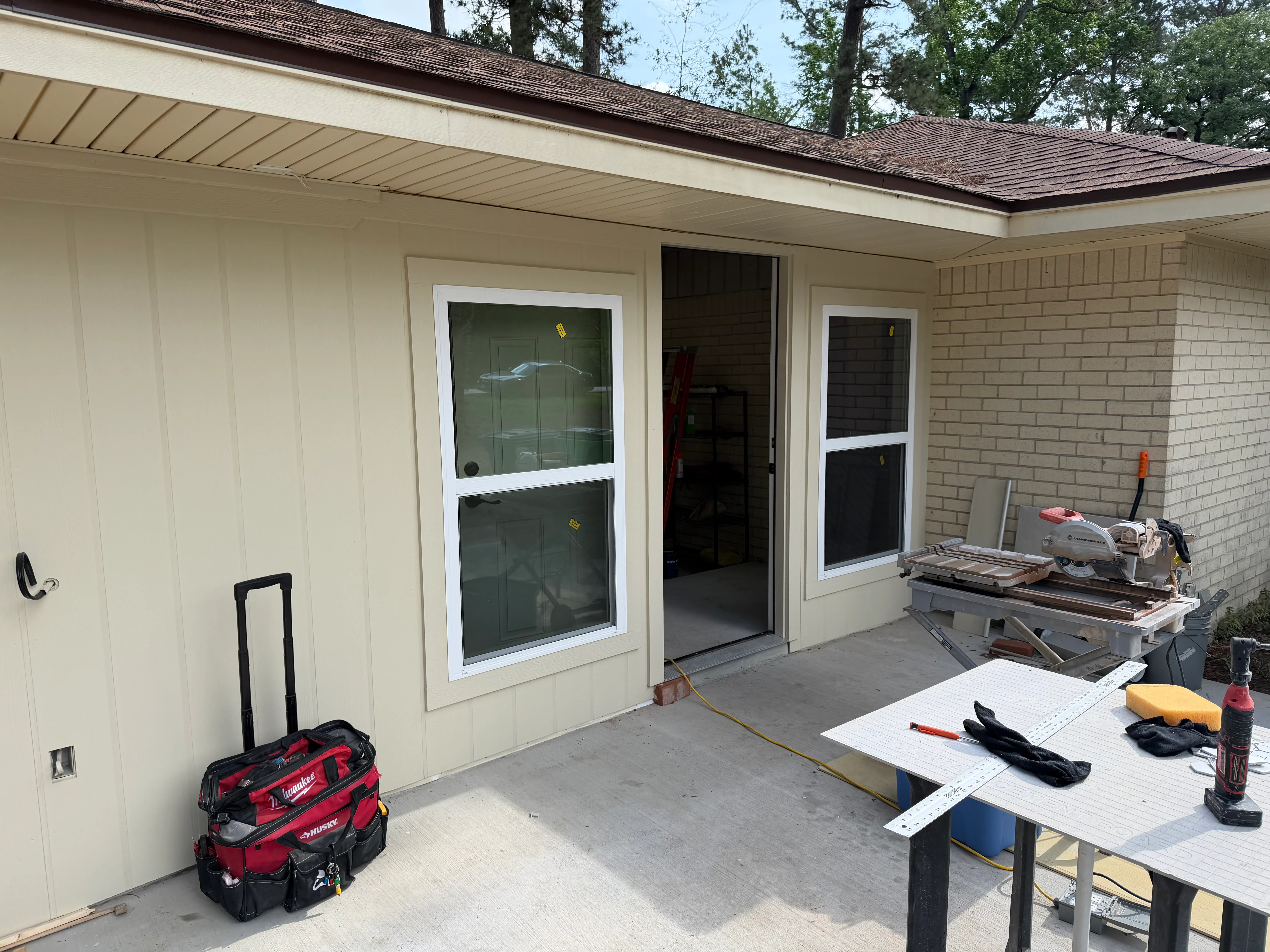 New garage addition with cream vinyl siding, dark roof shingles, and white-framed windows during construction phase
