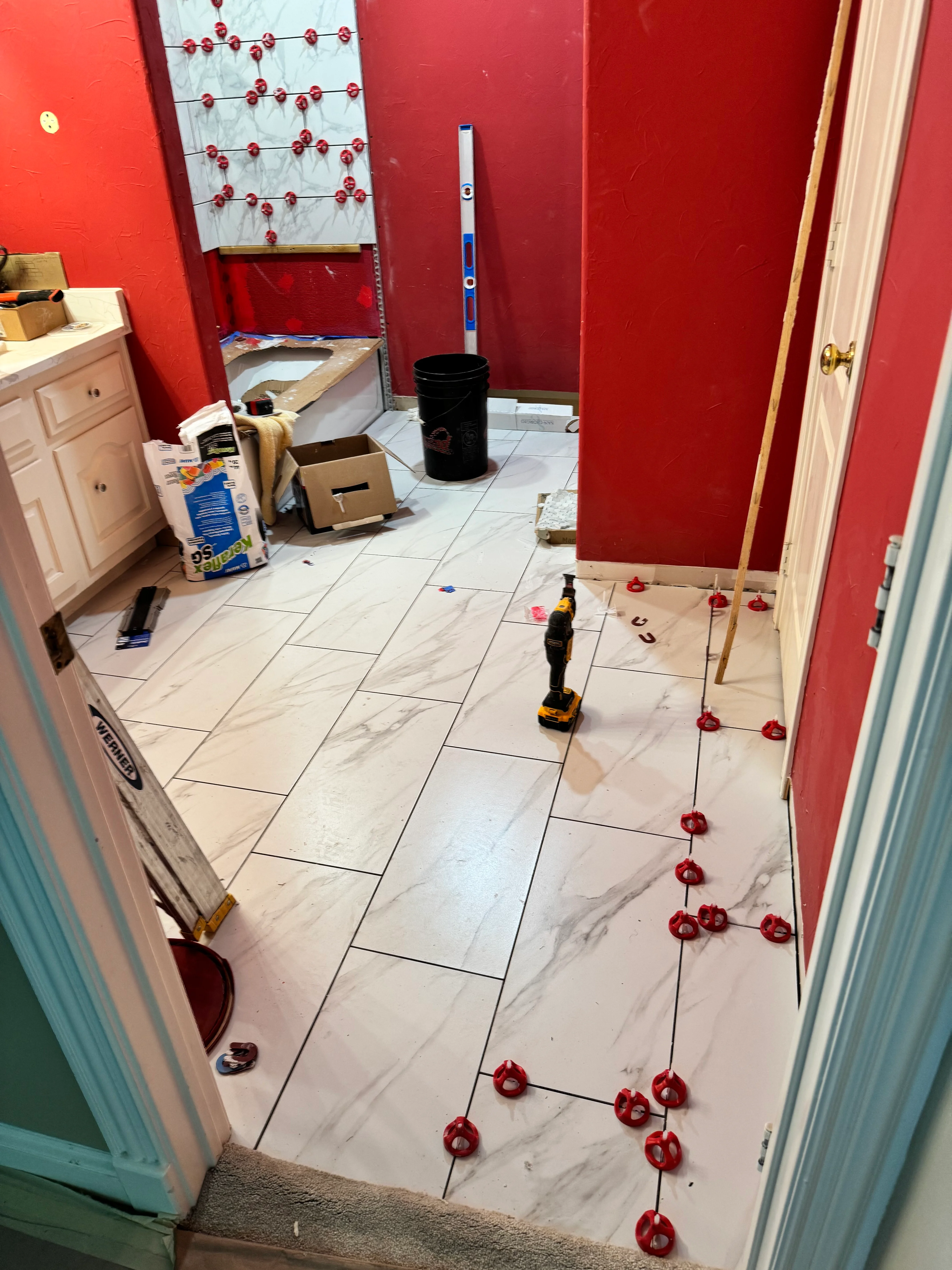 Bathroom under renovation with marble-look tile flooring and red accent walls
