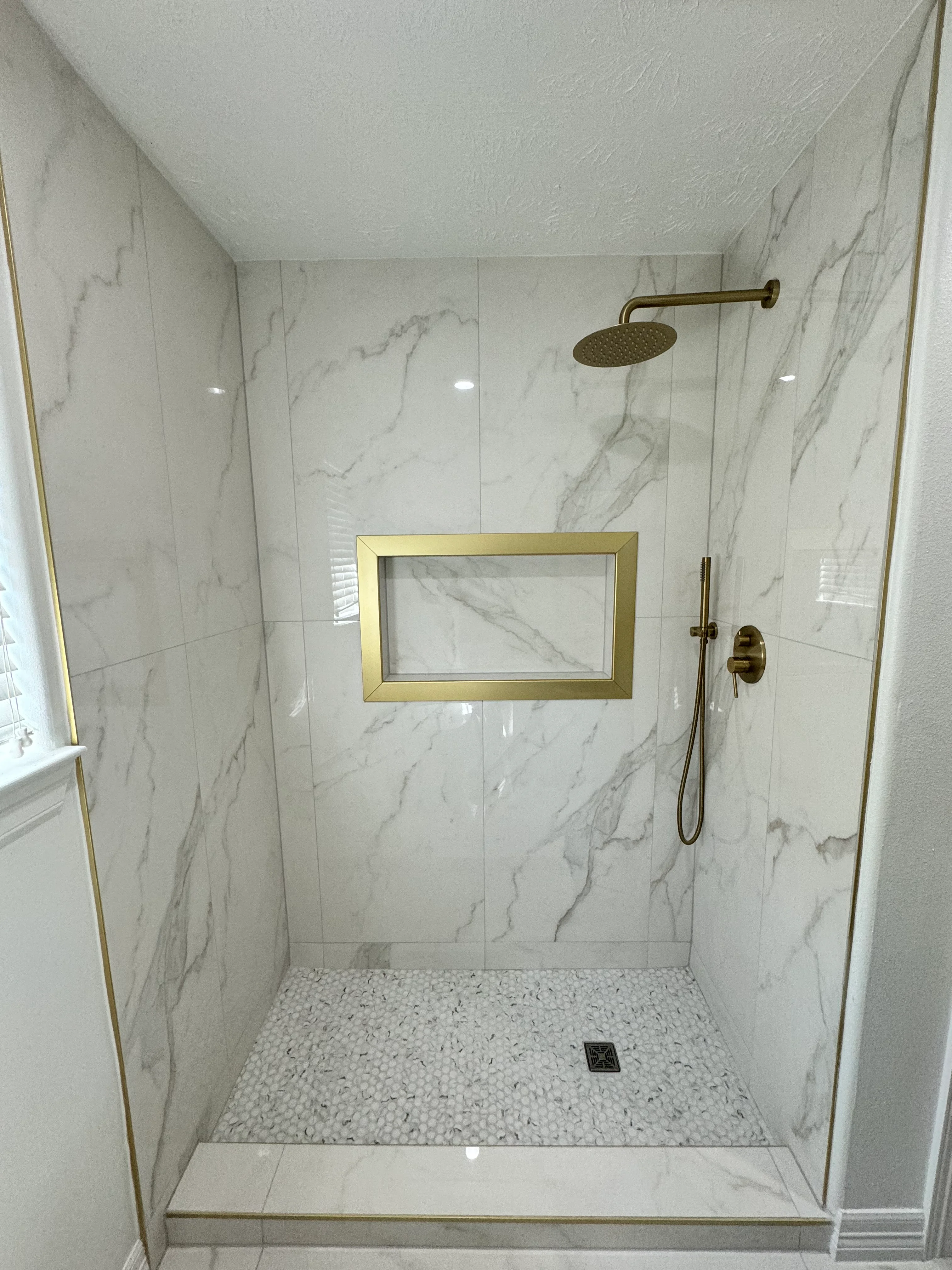 Modern shower with marble tile walls, brass fixtures, and pebble stone floor