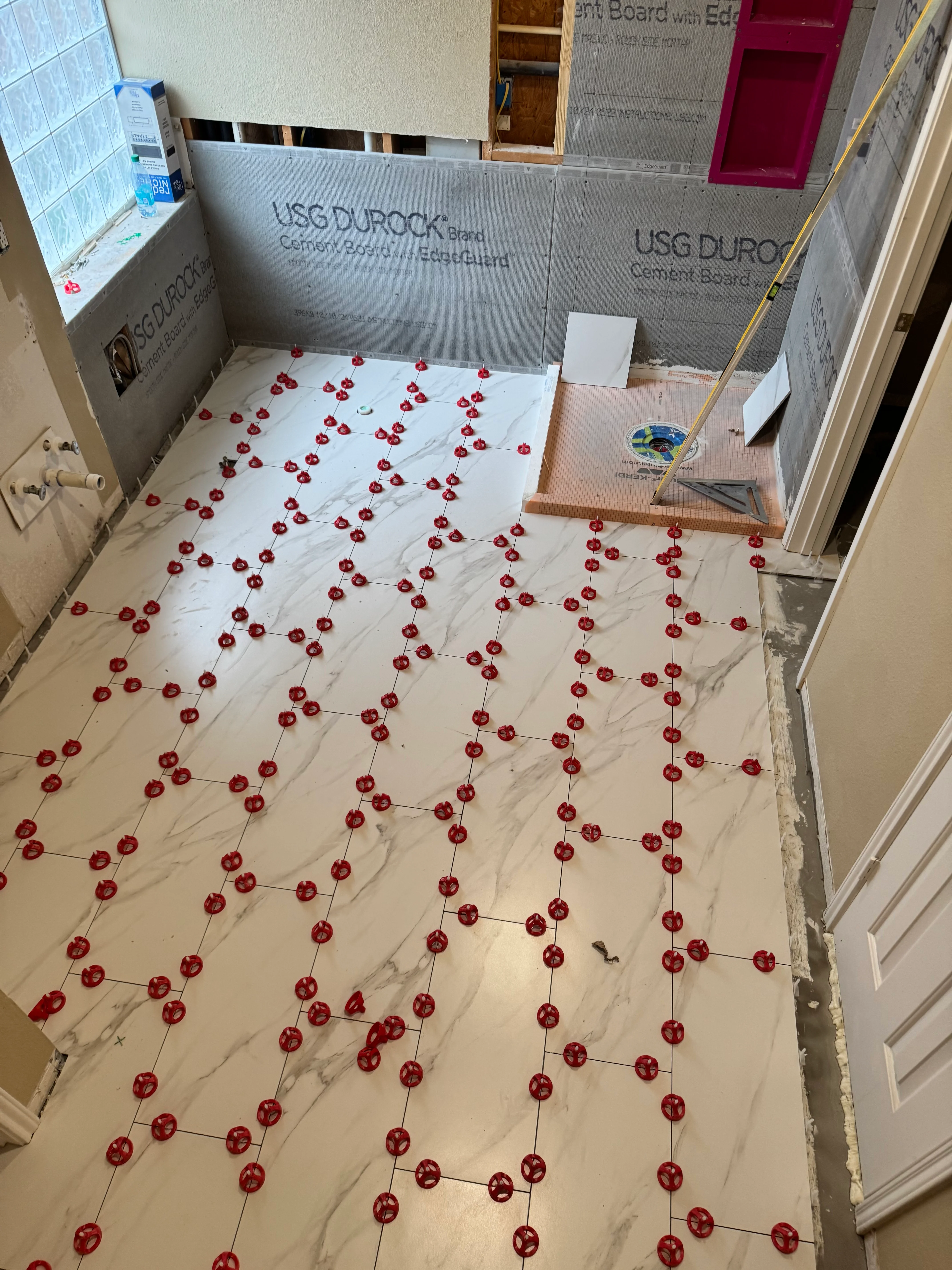 Bathroom floor with marble-look porcelain tiles and red spacers laid out for installation