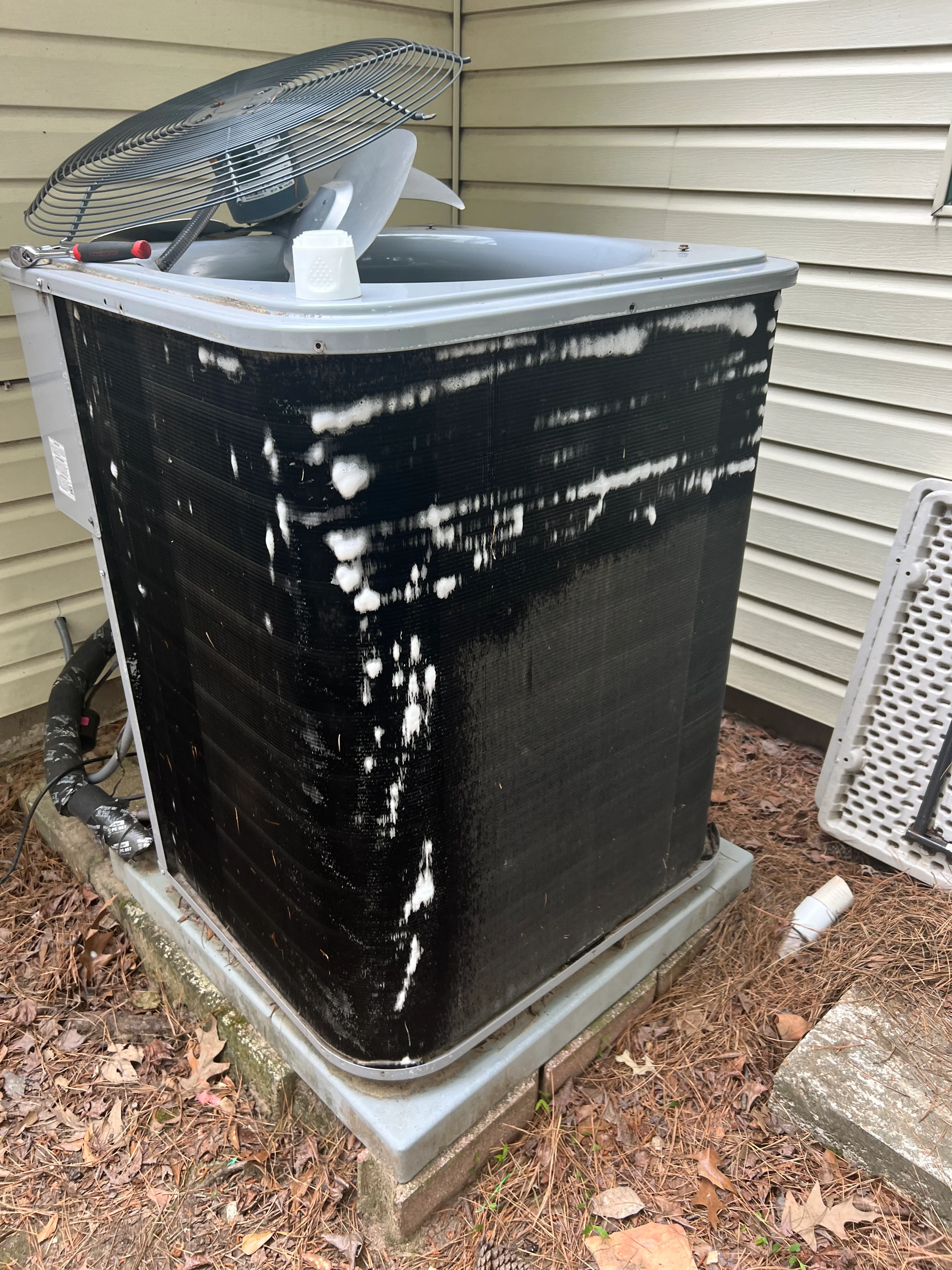 Black AC condenser unit with white algae buildup on coils being serviced