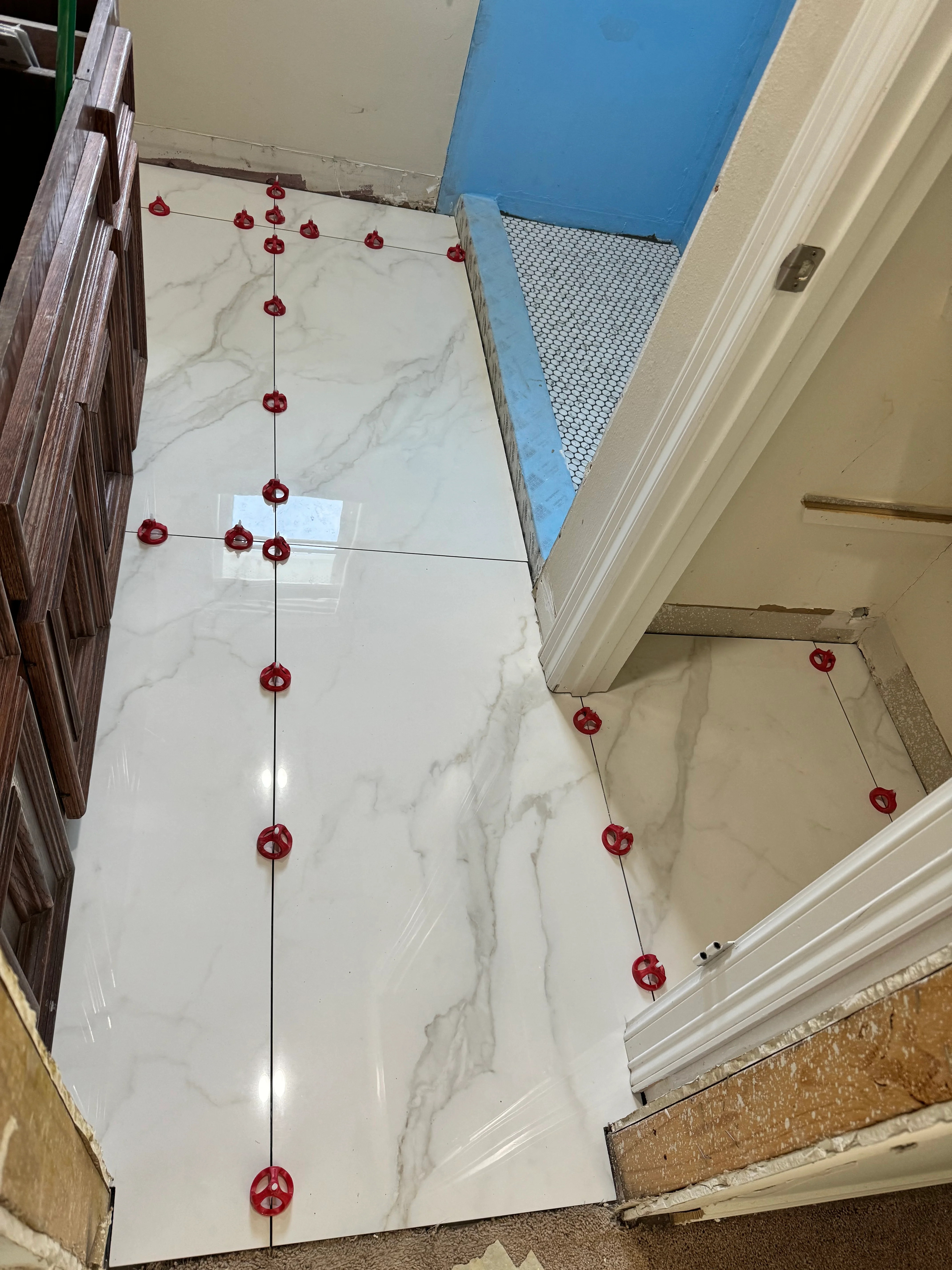 Marble porcelain tiles with red spacer guides marking layout lines for bathroom installation
