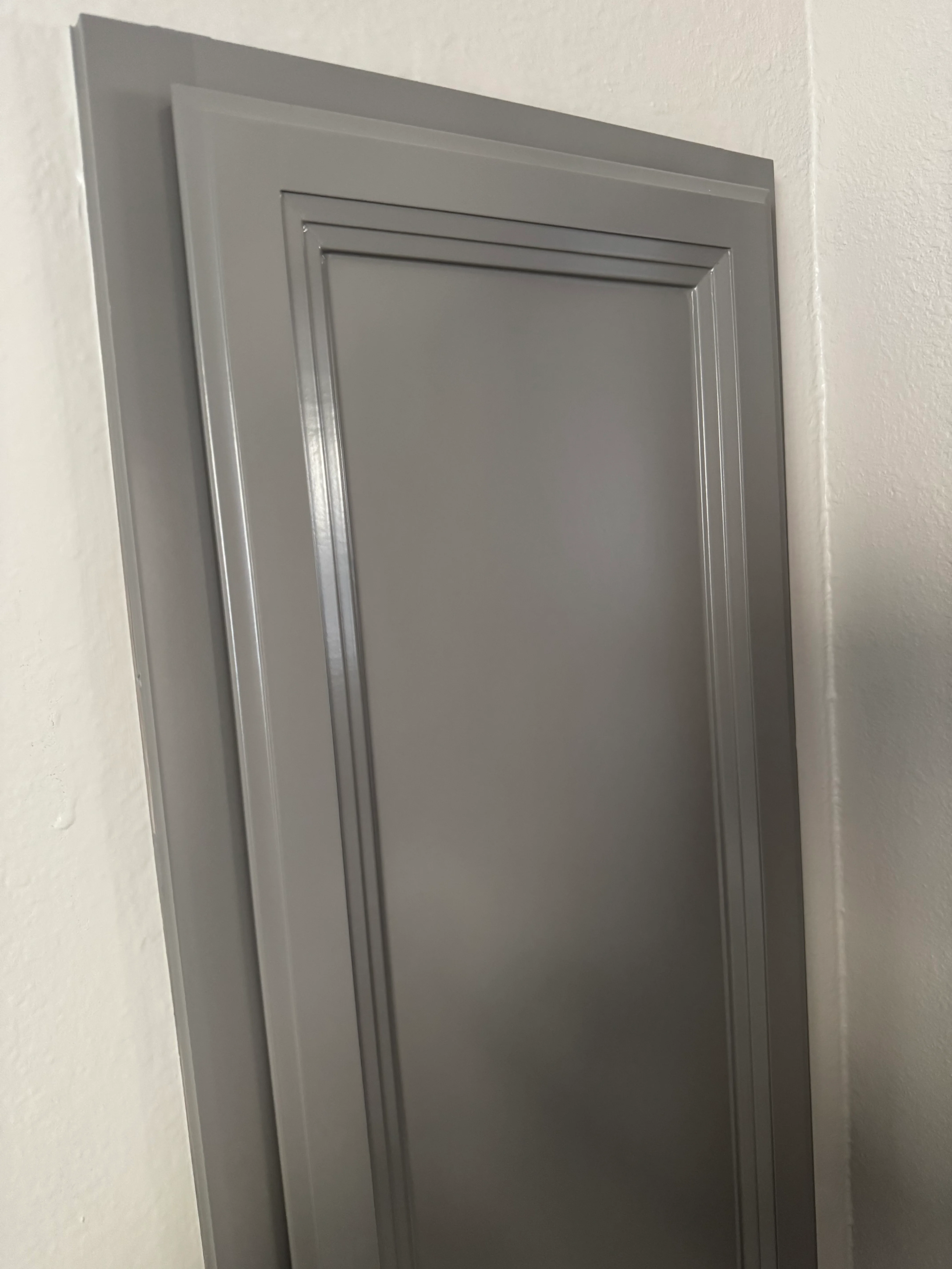 Gray interior door with recessed panel design and trim molding installed in white drywall