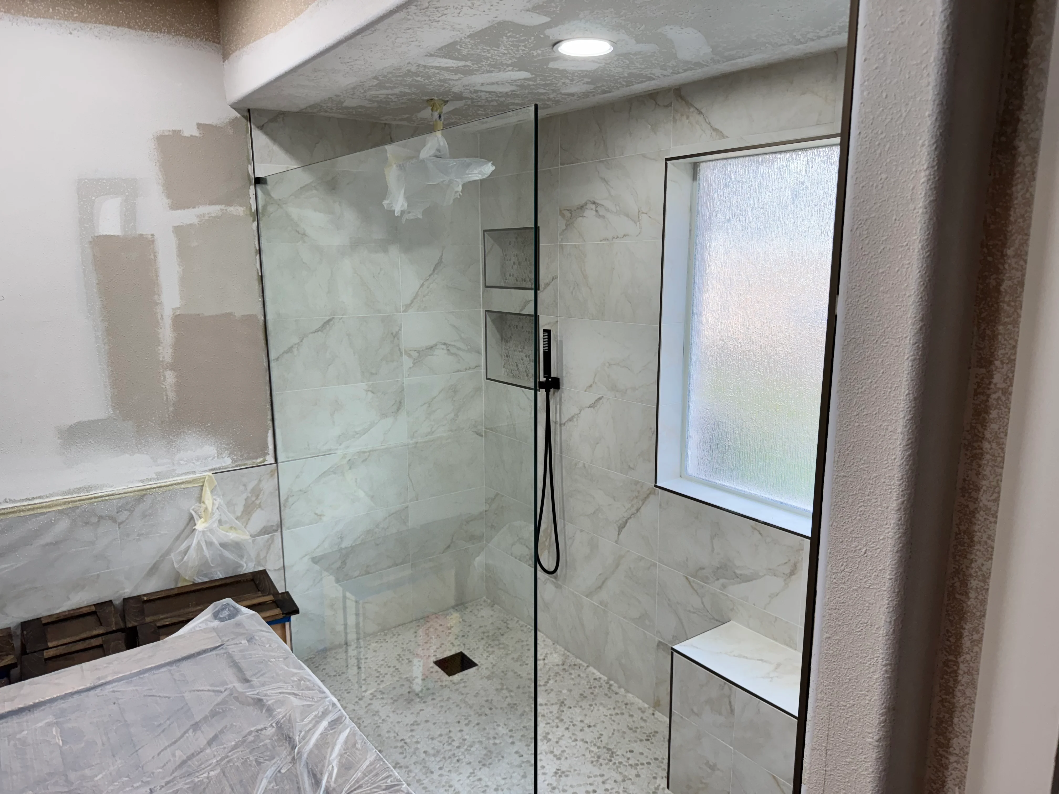 Modern walk-in shower with marble tile, frameless glass doors, and black fixtures