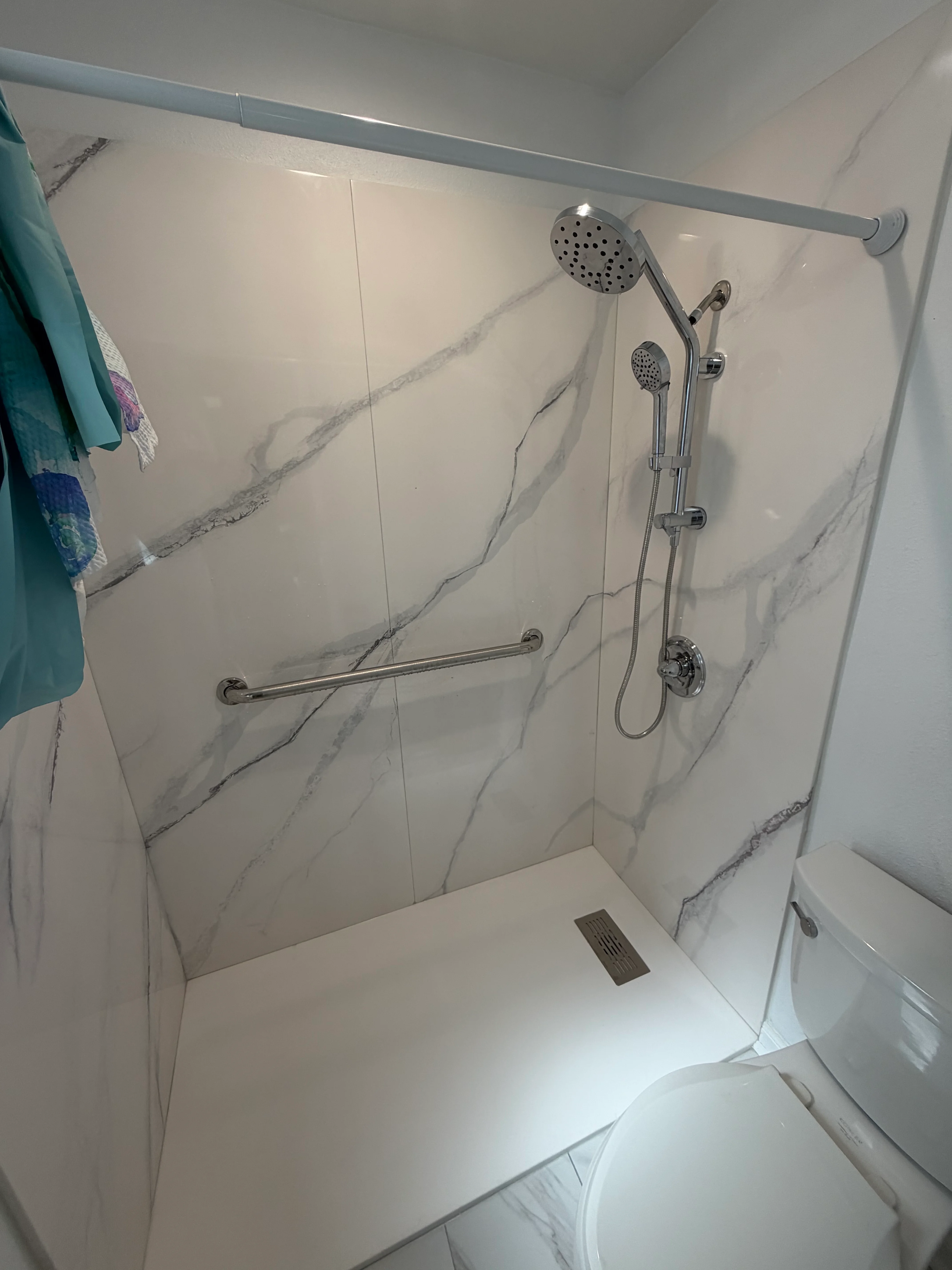 Newly remodeled shower with marble-look tile walls, dual showerheads, and chrome fixtures