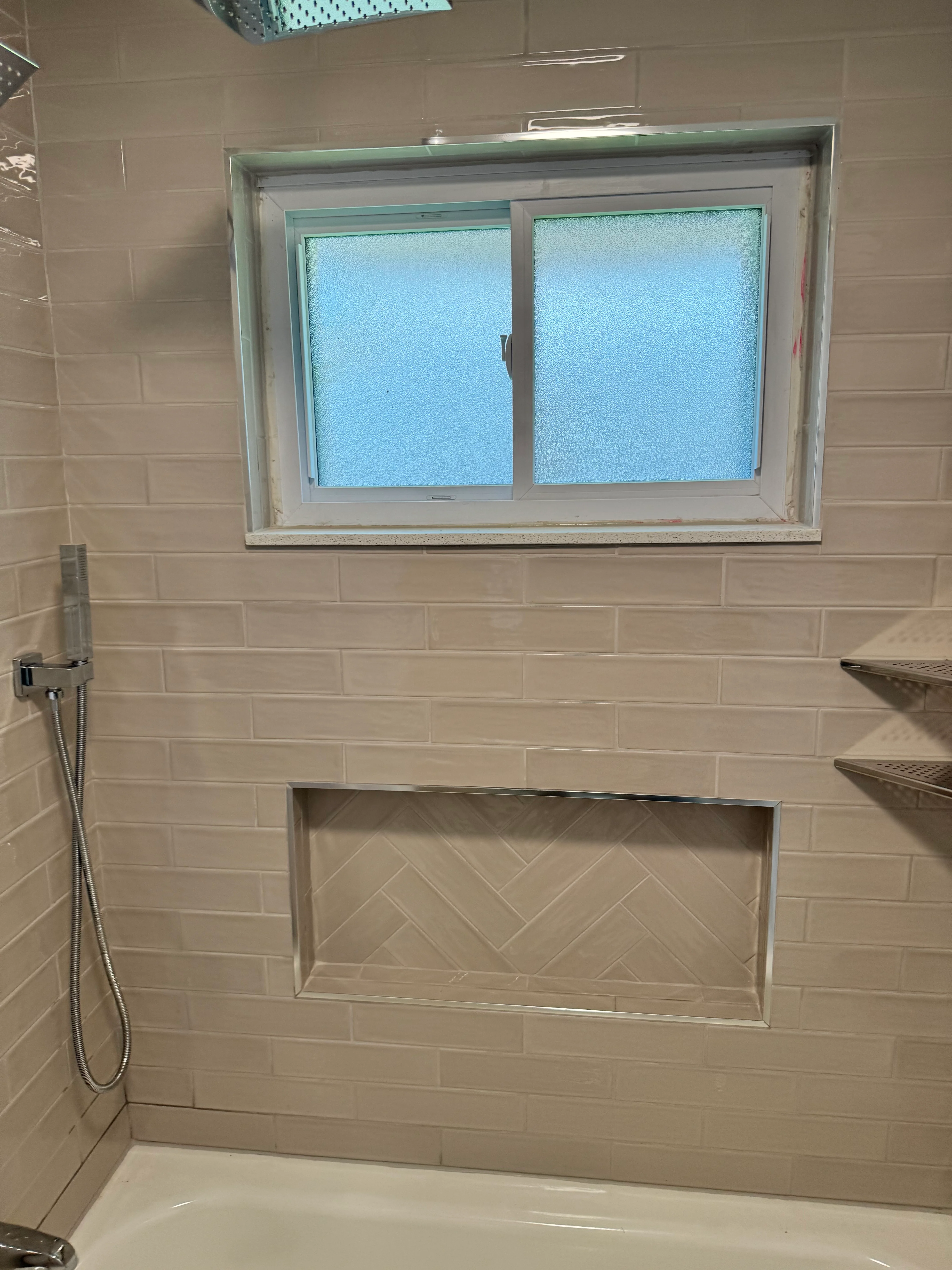 Bathroom with cream subway tile walls, frosted window, and herringbone niche detail