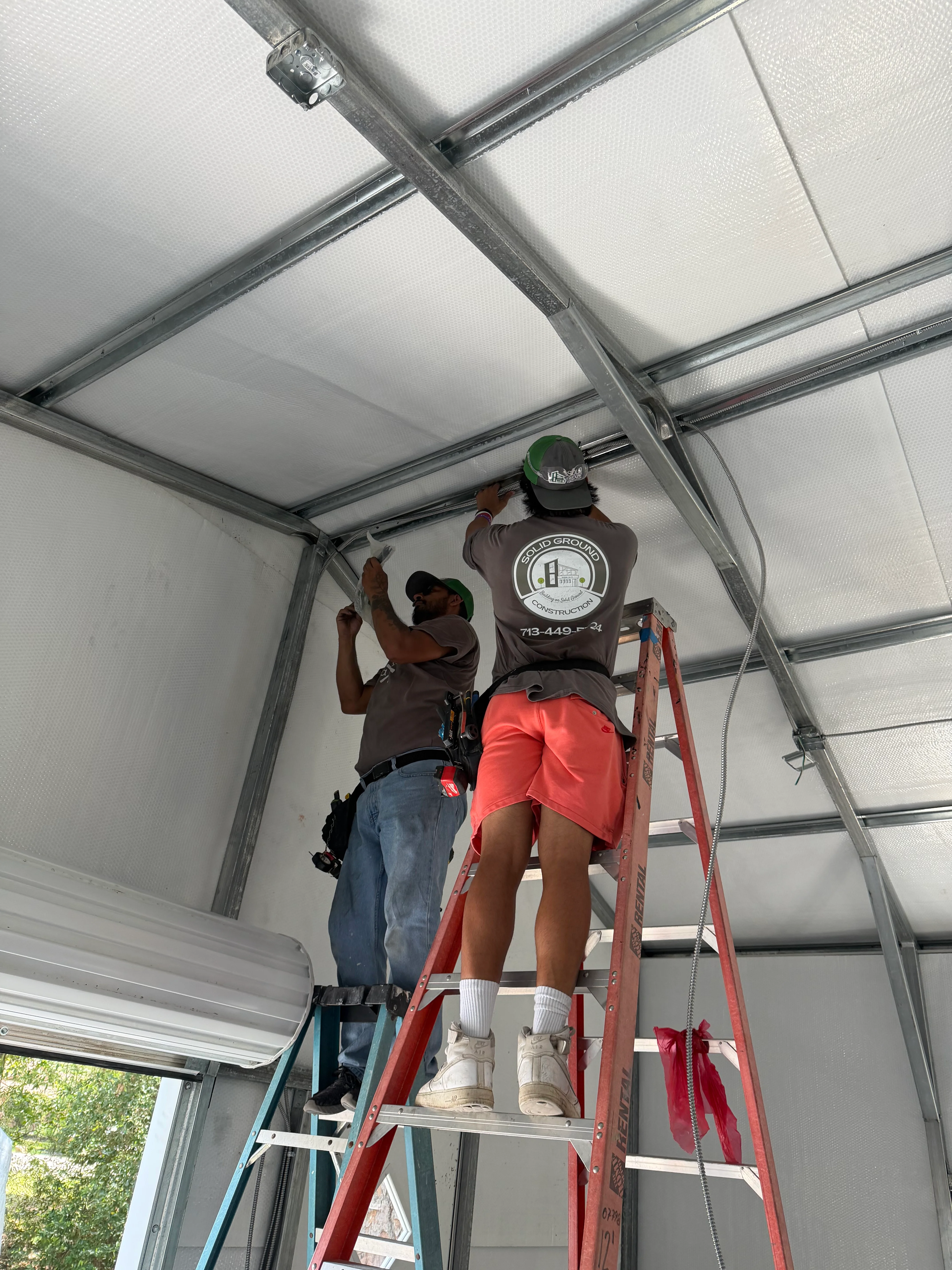 Two technicians installing polycarbonate garage door panels on steel frame structure