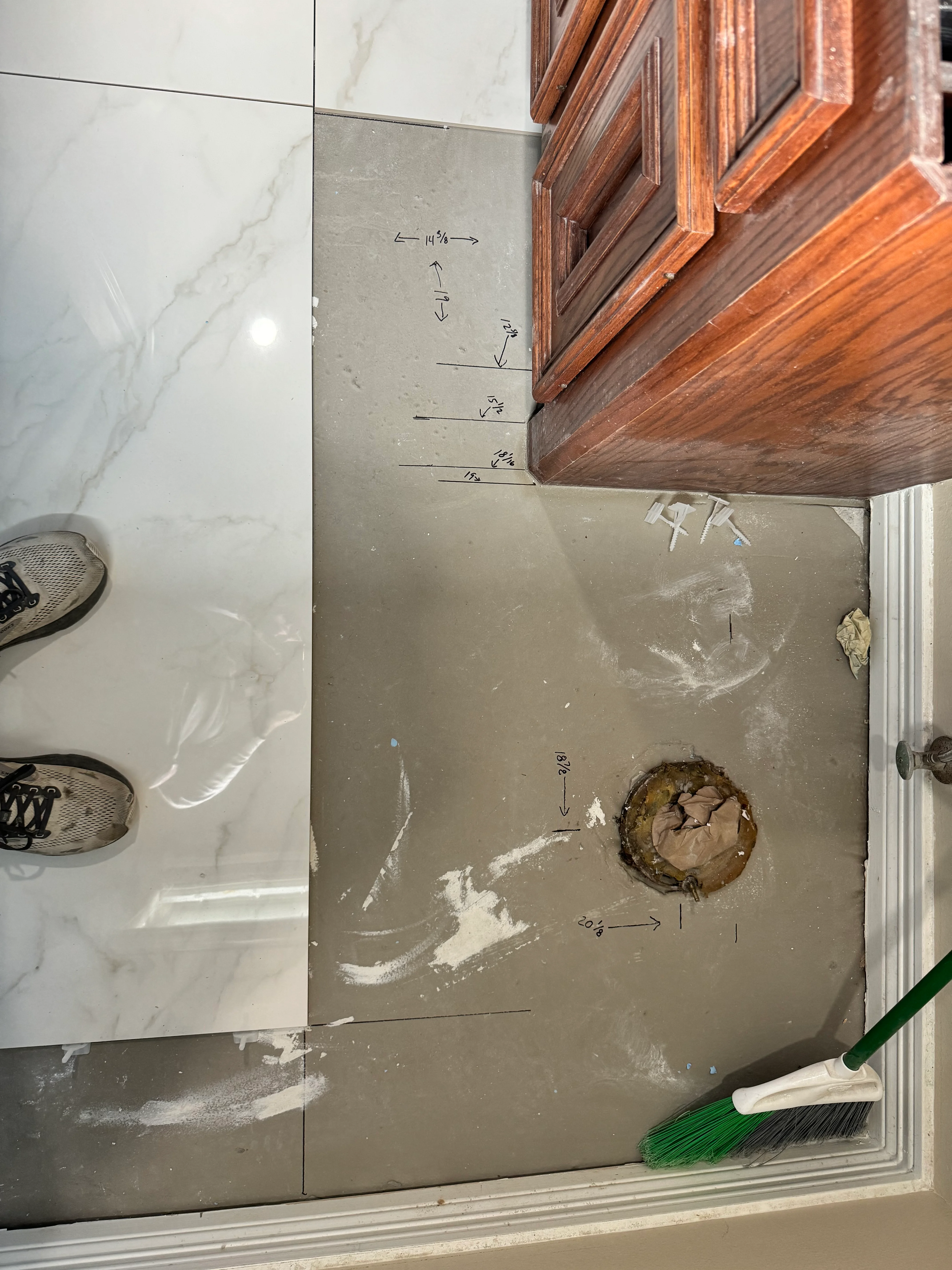 Bathroom floor with concrete substrate, tile layout markings, and marble-look porcelain tiles during installation