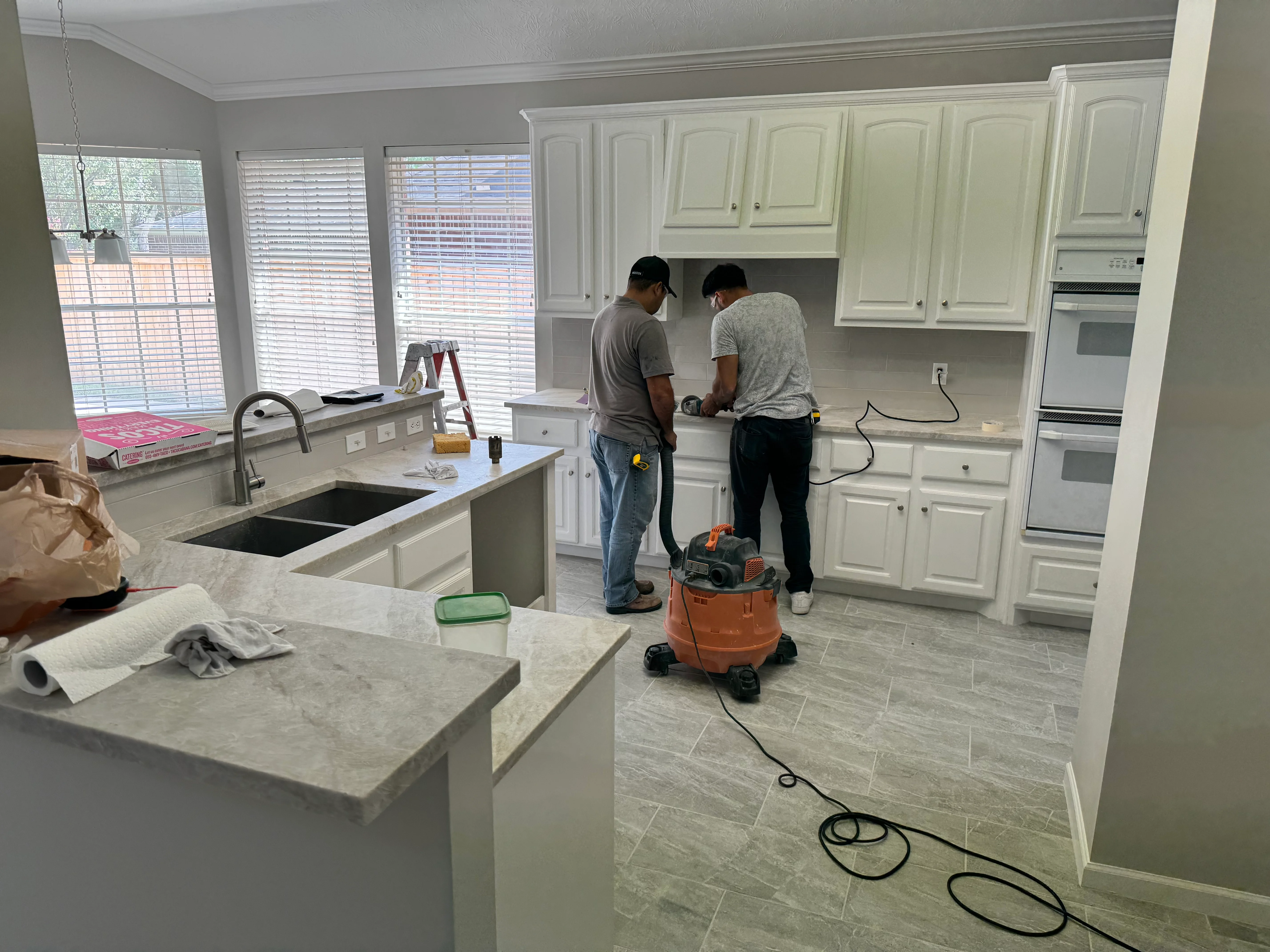 Two workers installing white kitchen cabinets and countertops during active remodel project