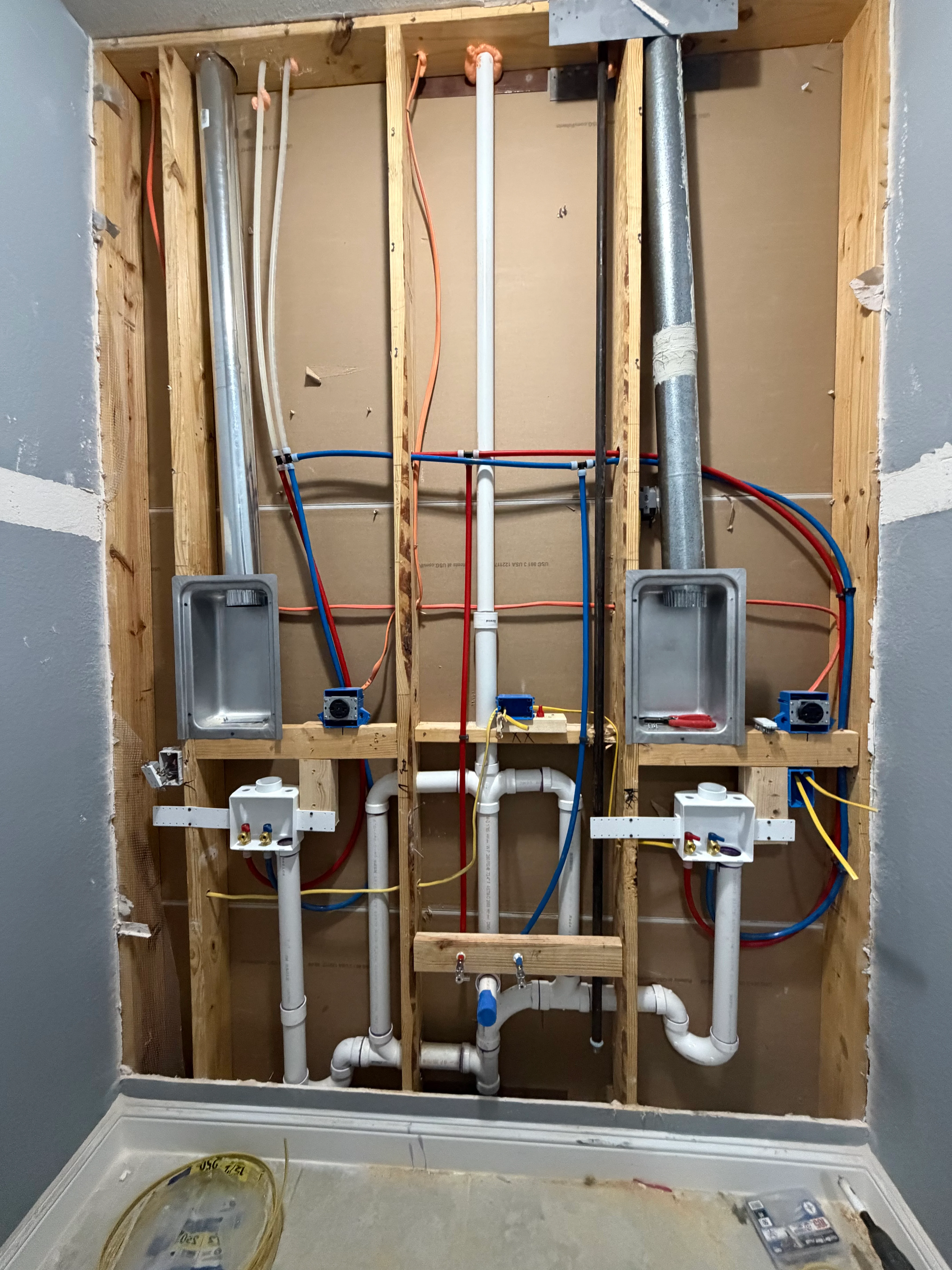 Dual bathroom rough-in plumbing with copper pipes, PVC drains, and electrical boxes in framed wall