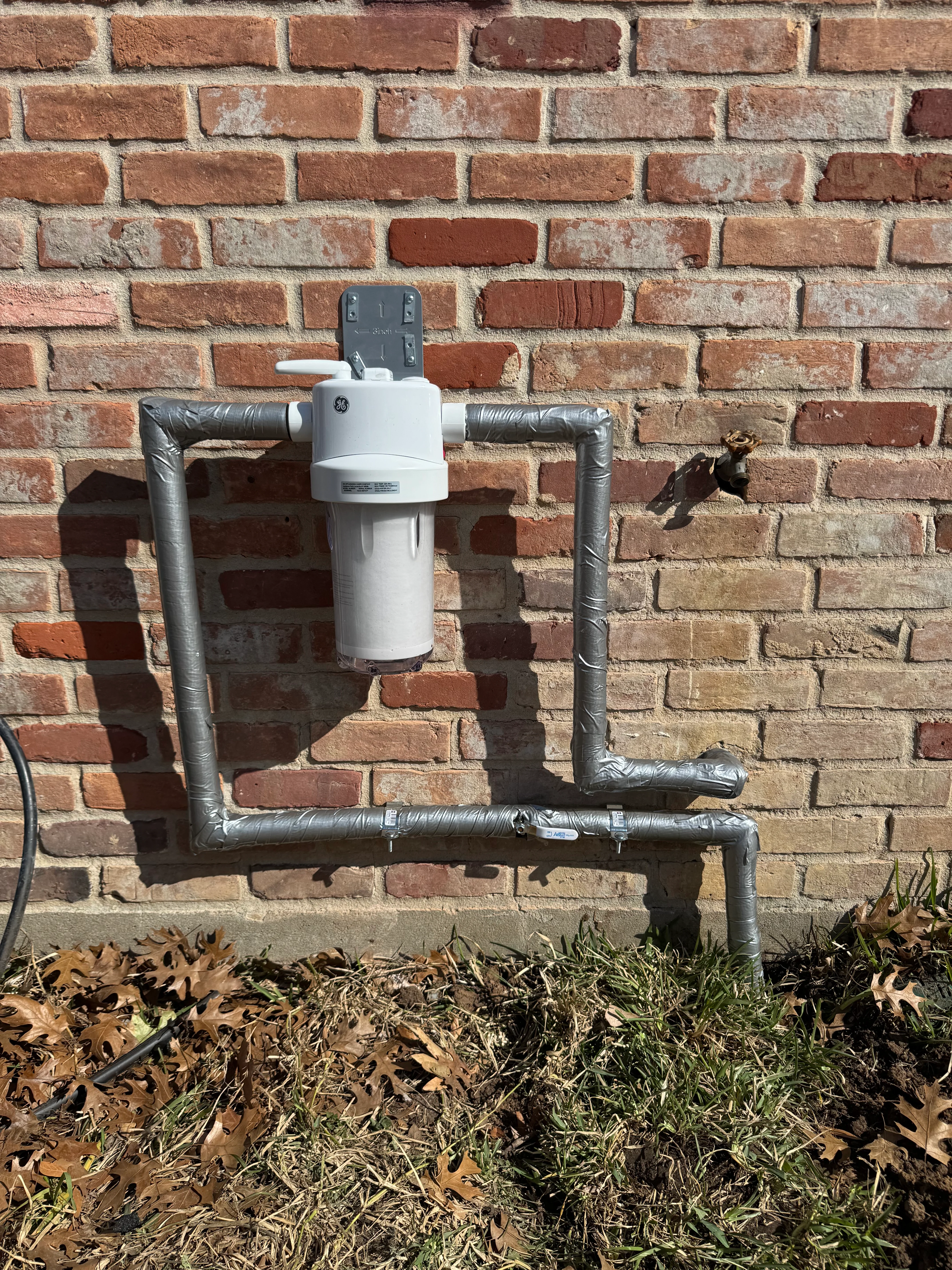 Whole-home water filter with insulated copper pipes mounted on brick exterior wall