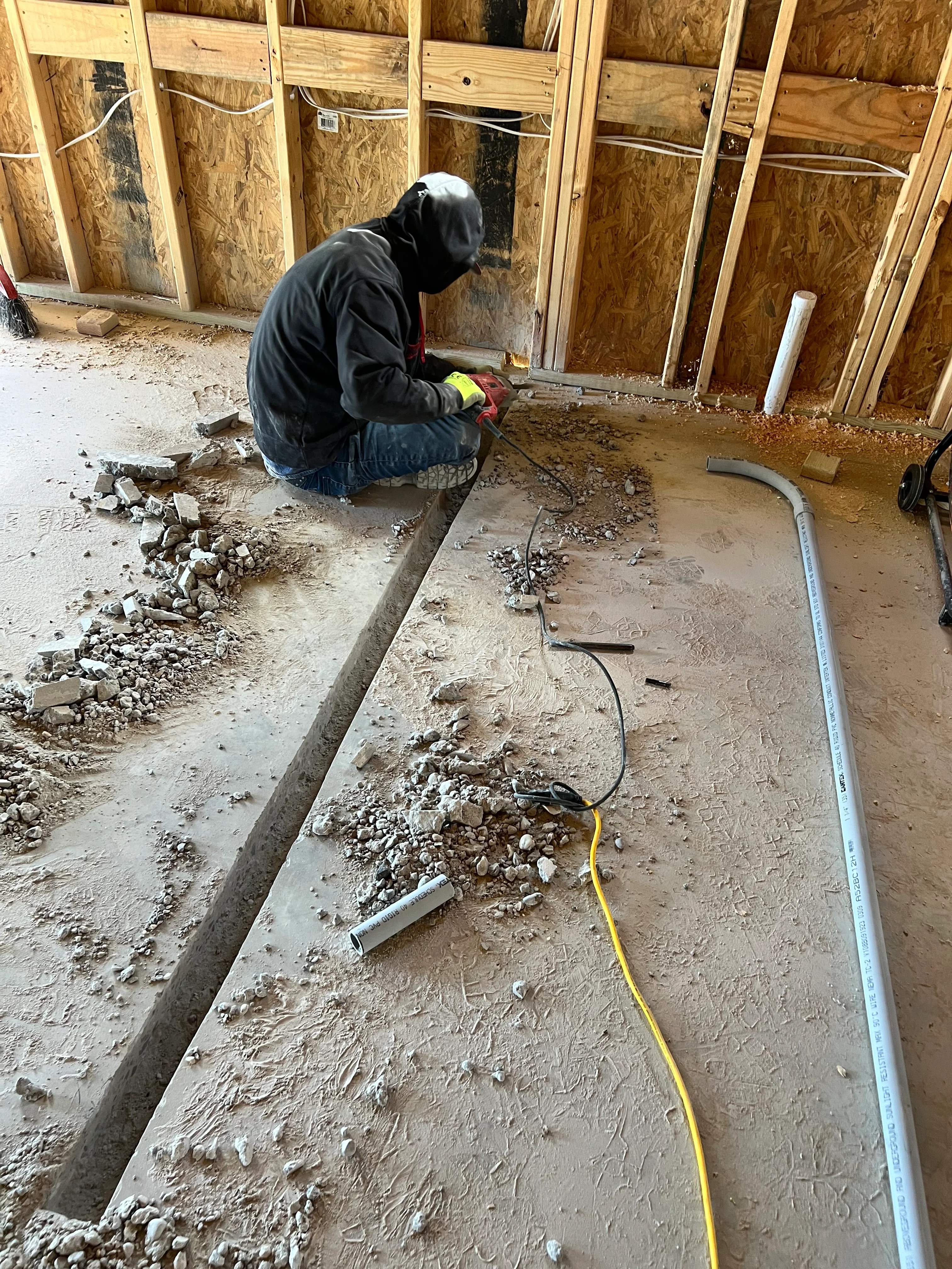 Worker installing utilities in freshly poured concrete foundation with PVC and electrical conduit