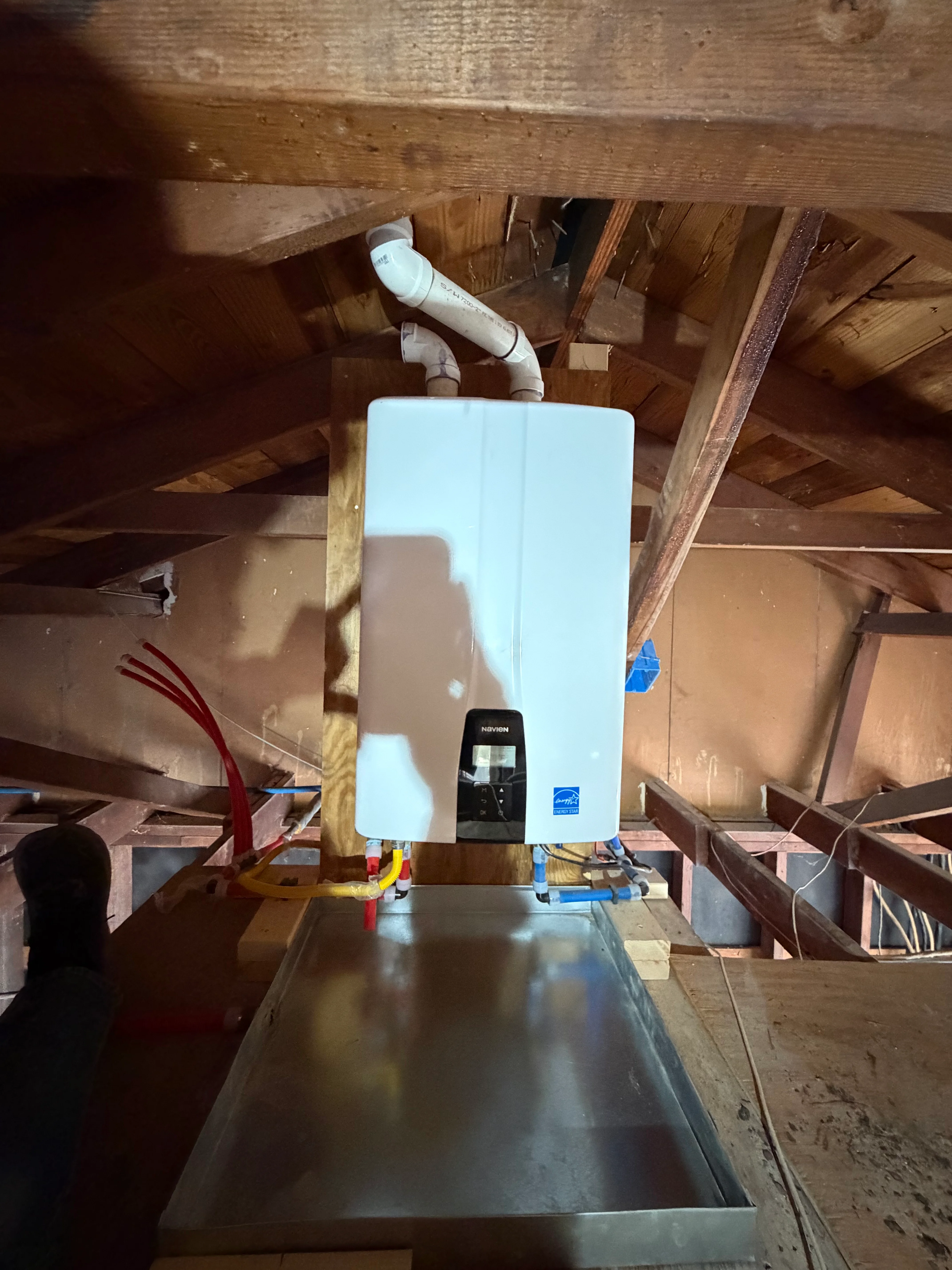 Tankless water heater mounted in attic with white venting pipe and electrical connections