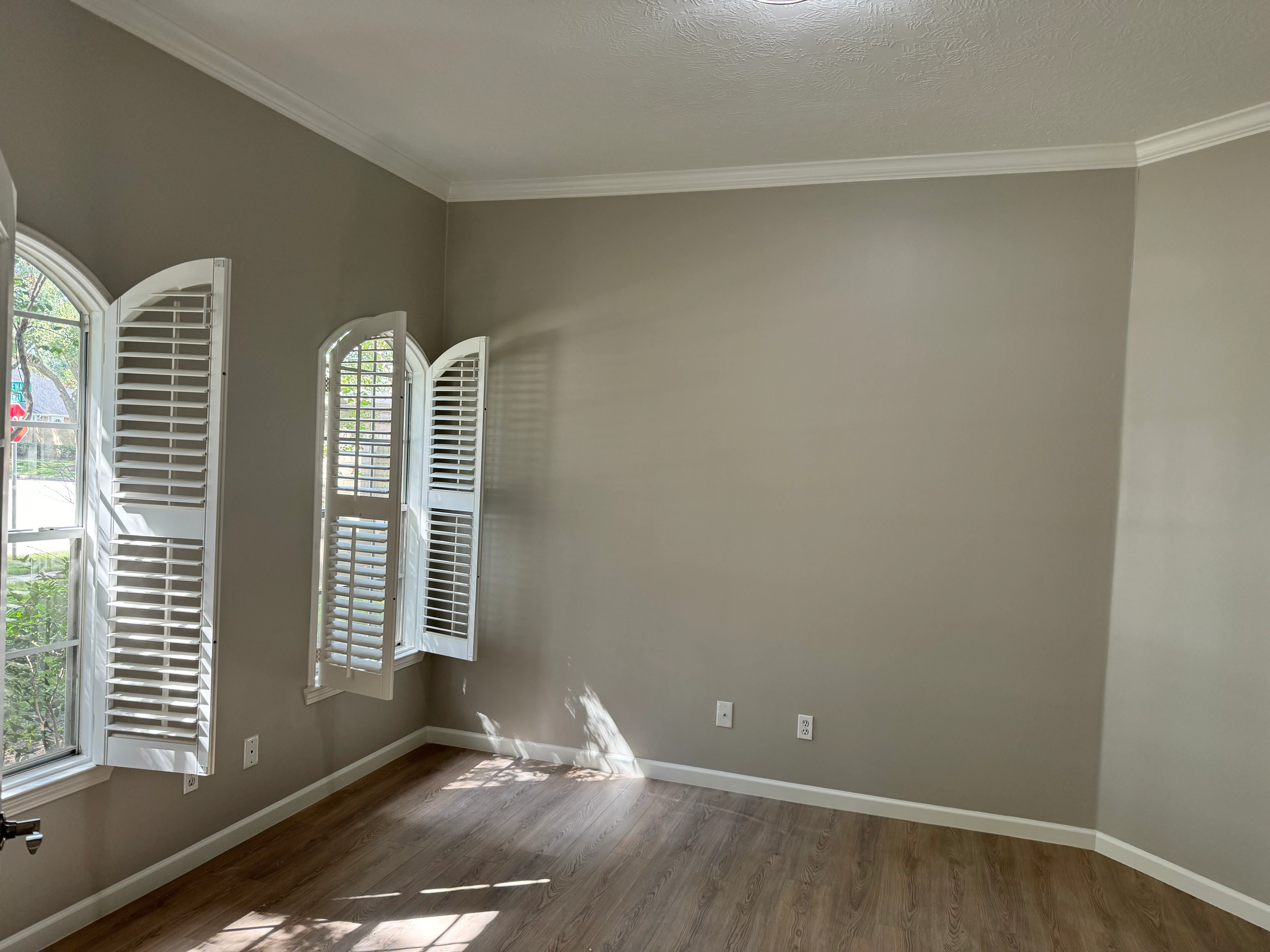 Remodeled bedroom with taupe walls, crown molding, hardwood floors, and white plantation shutters