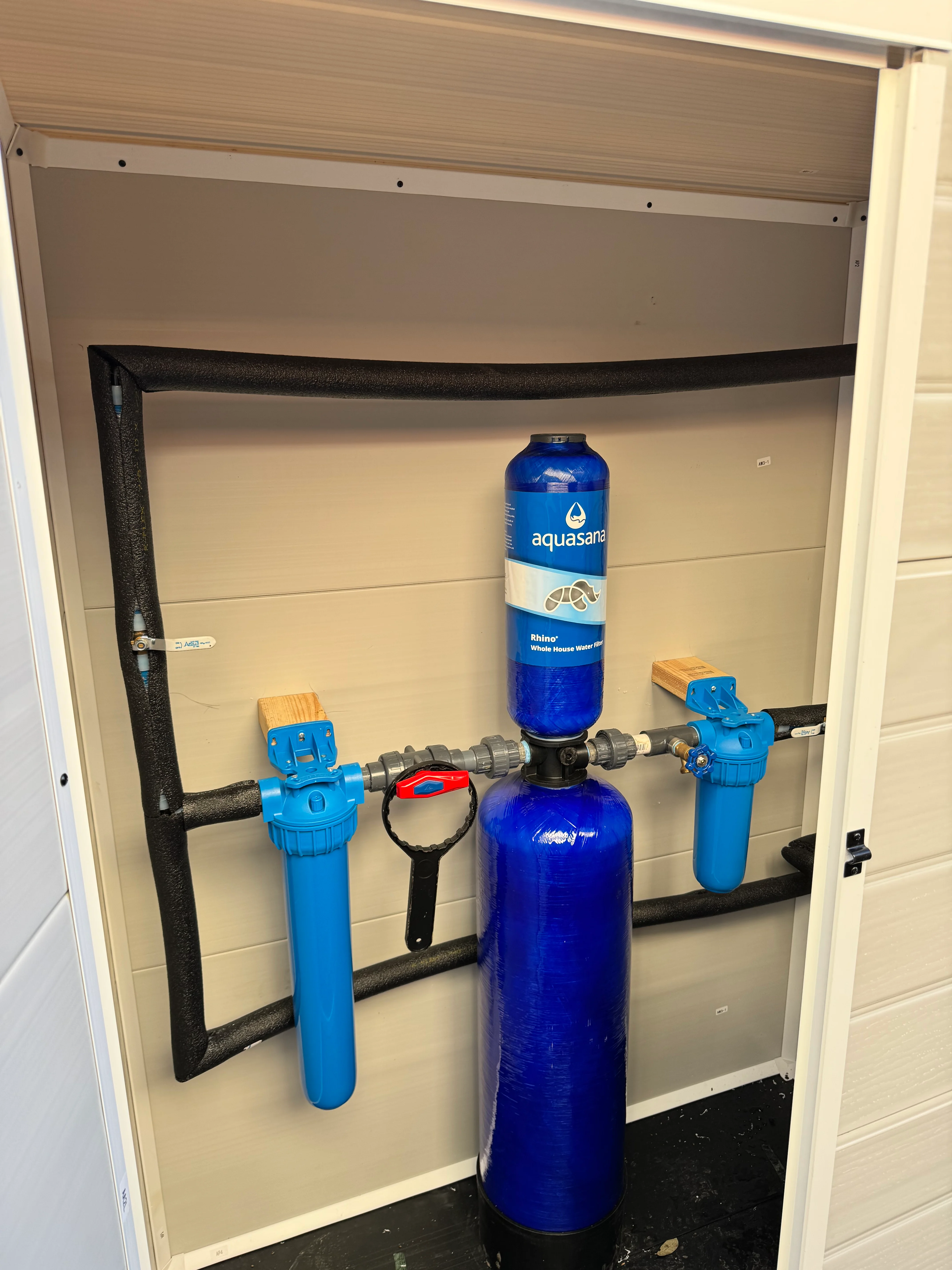 Installed whole-house water filtration system with dual blue tanks and blue valves in utility closet