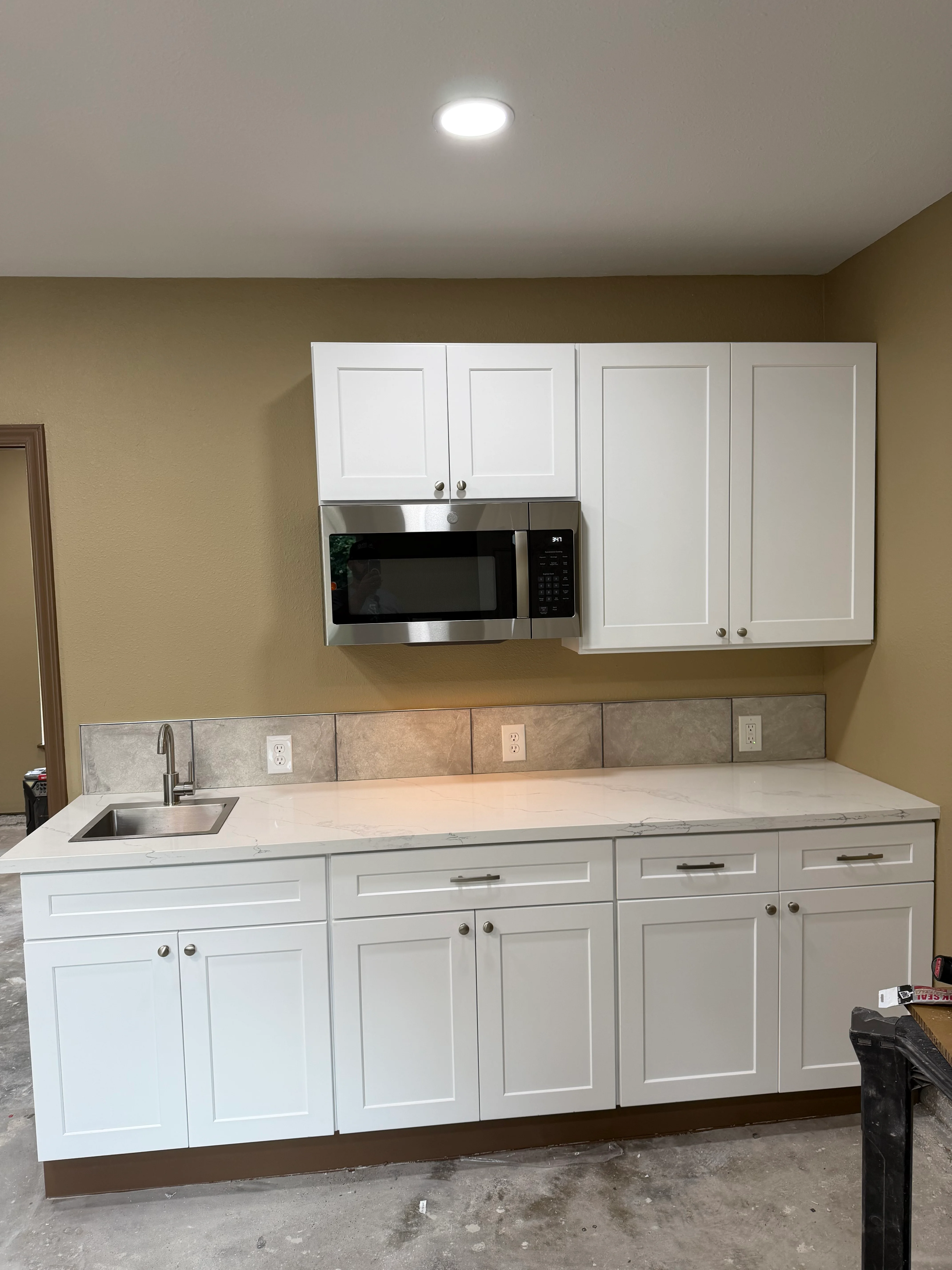 Modern kitchen with white cabinets, quartz countertops, stainless steel microwave, and tile backsplash