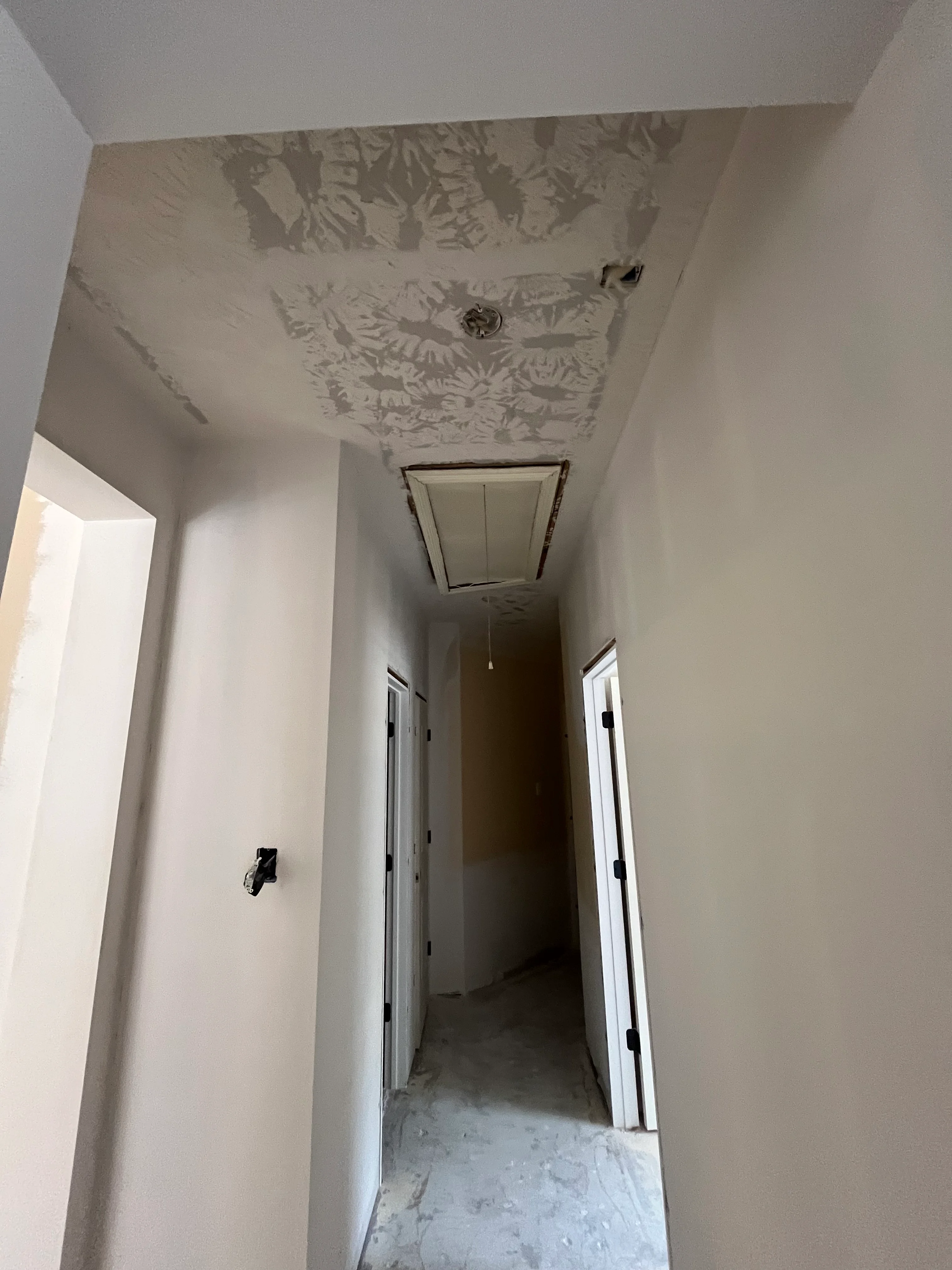 Newly finished hallway with white drywall, recessed ceiling light, and electrical outlets