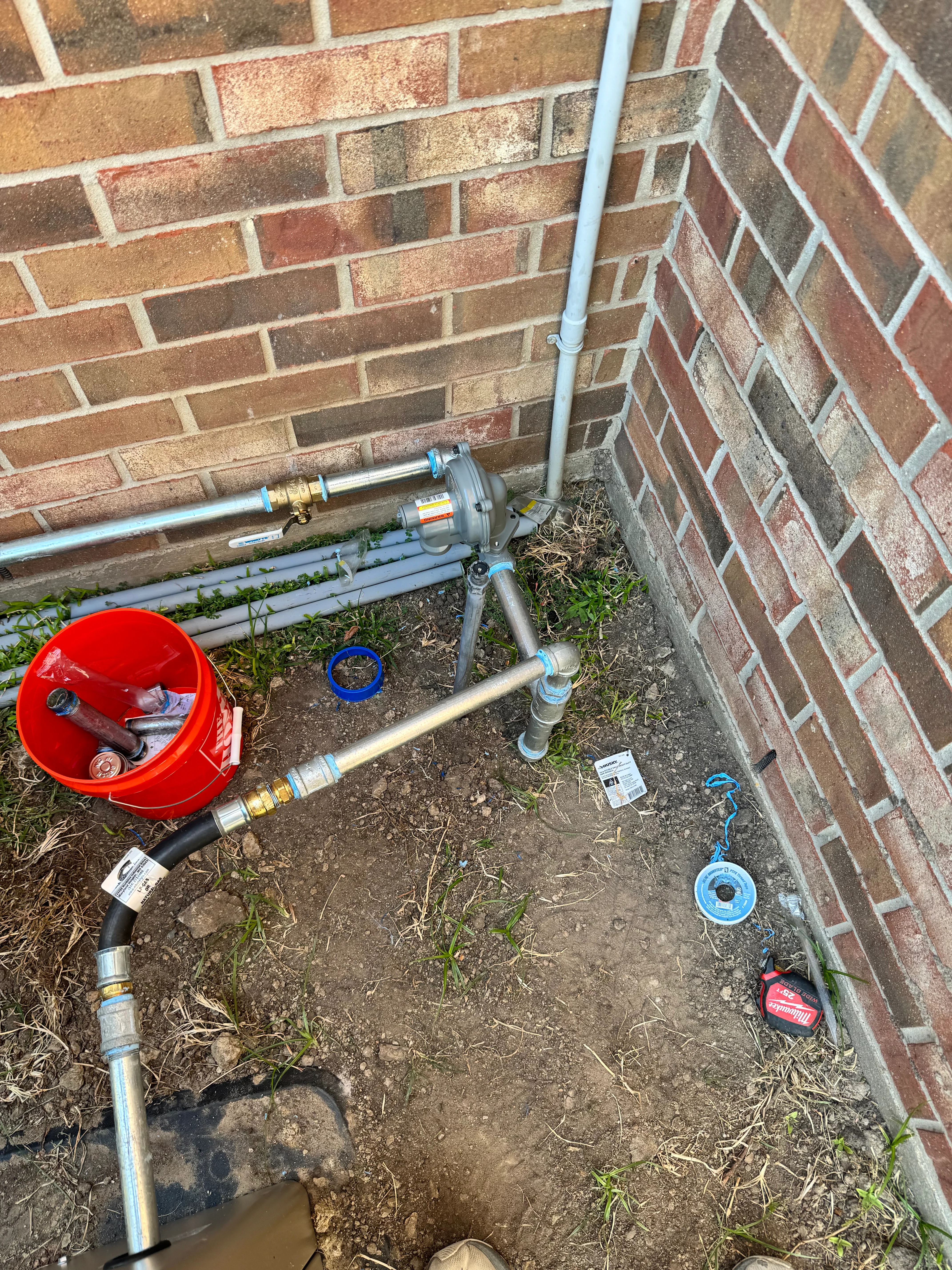 Exterior plumbing installation with copper and PVC pipes against brick wall