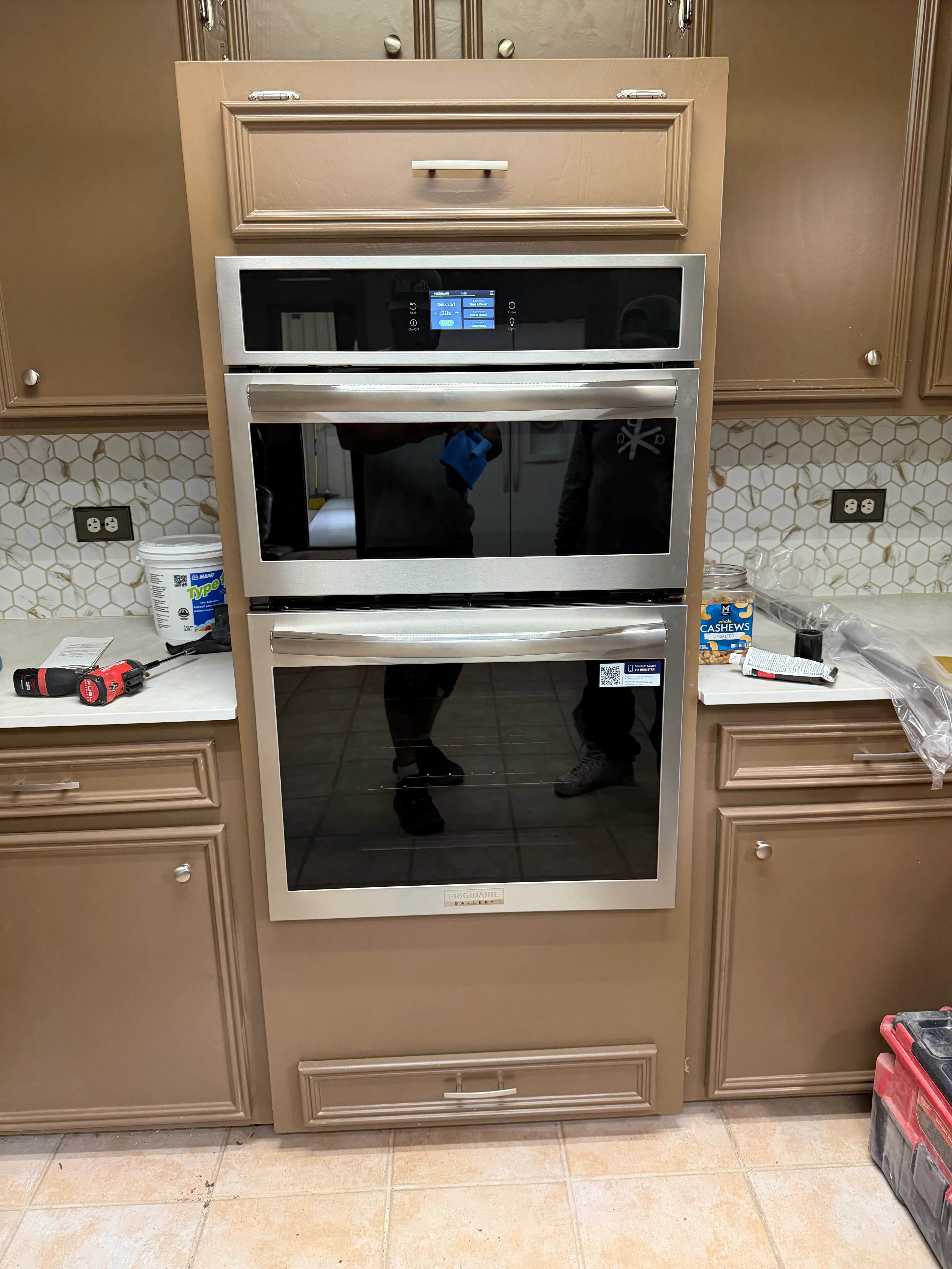Stainless steel double wall oven installed in tan kitchen cabinetry with hexagonal backsplash