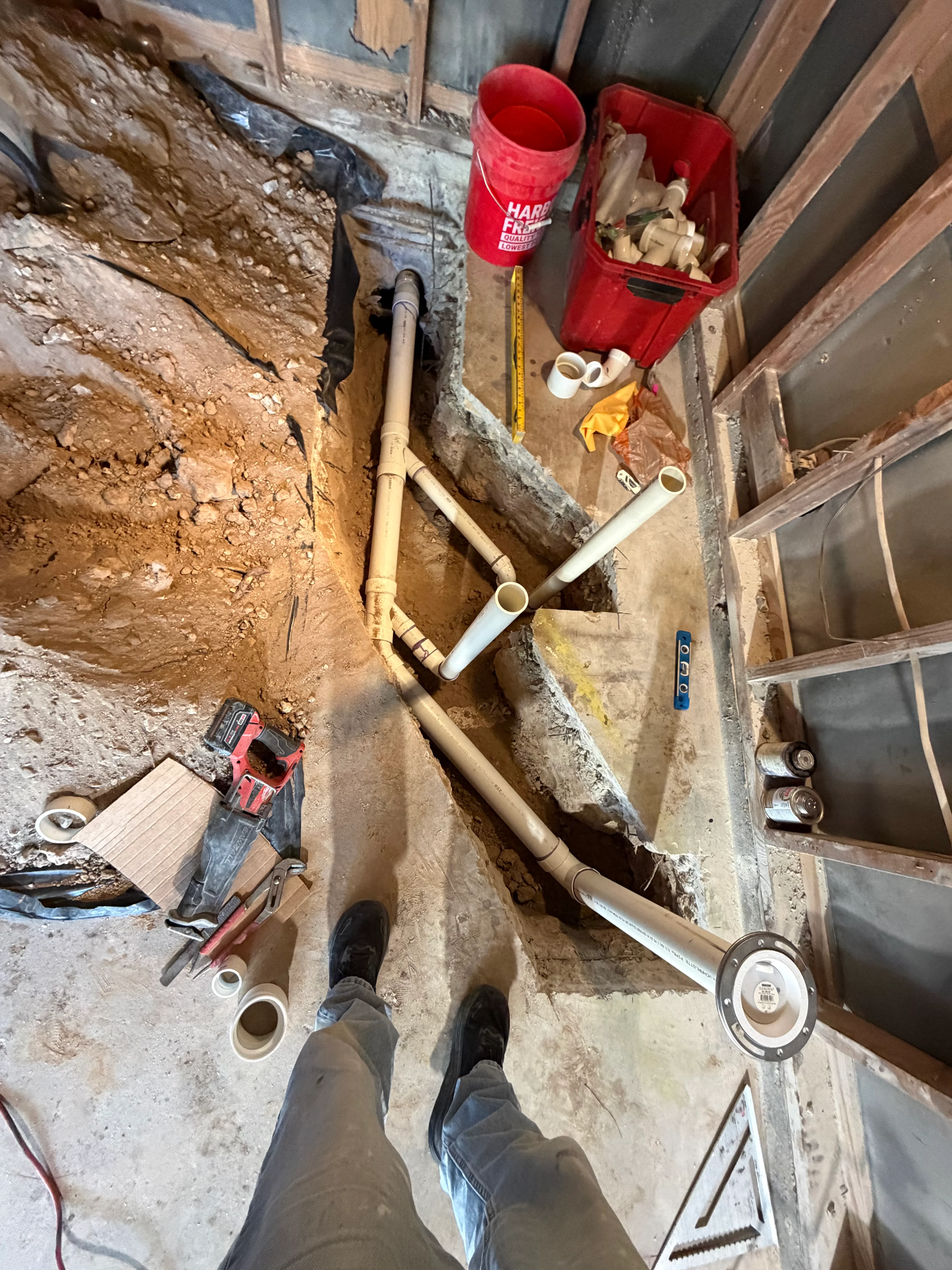 Basement plumbing installation with PVC and copper pipes, floor drains, and fittings