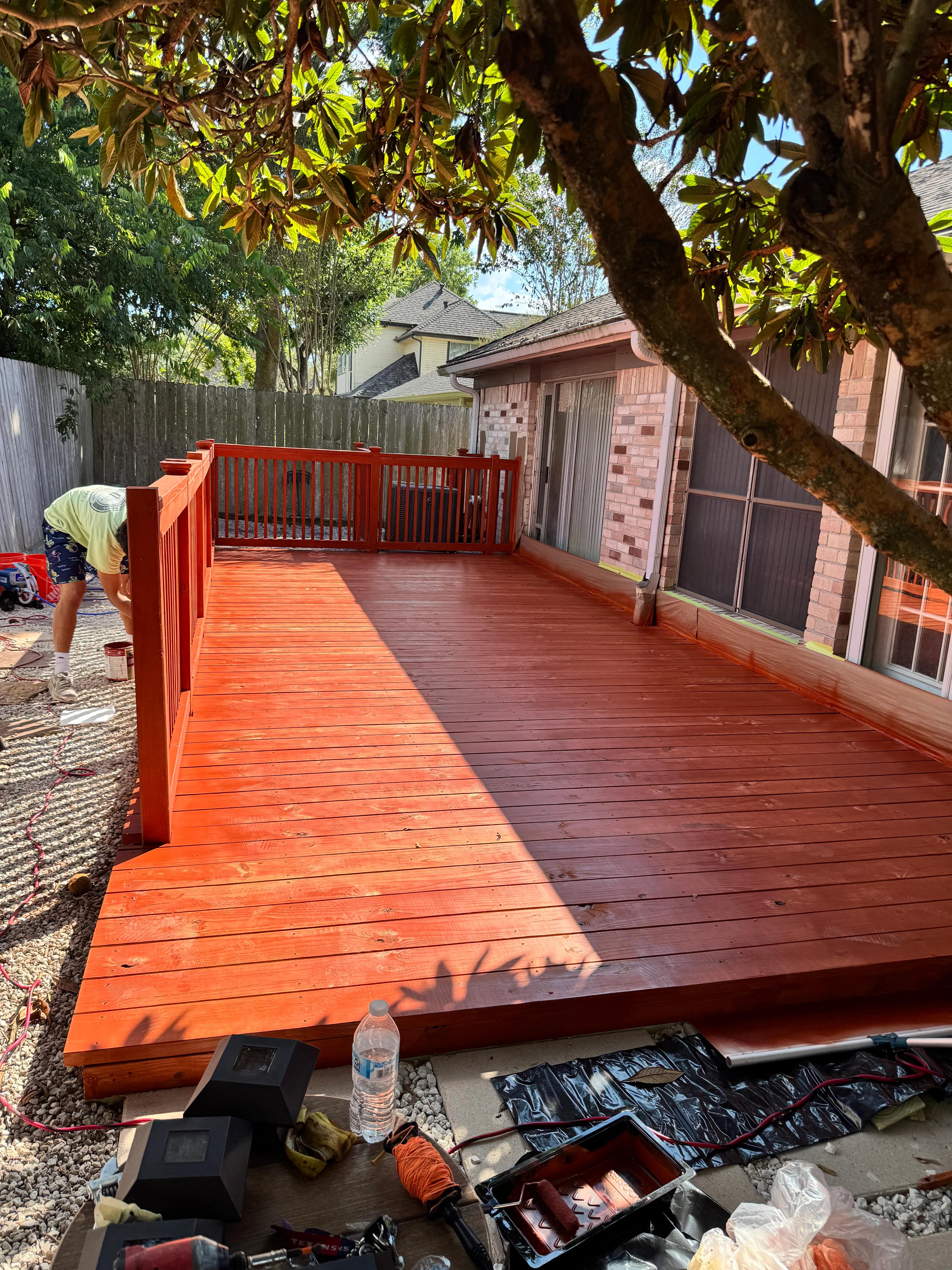 Two-tone composite deck with orange and burgundy boards, safety railings, and mature tree overhead