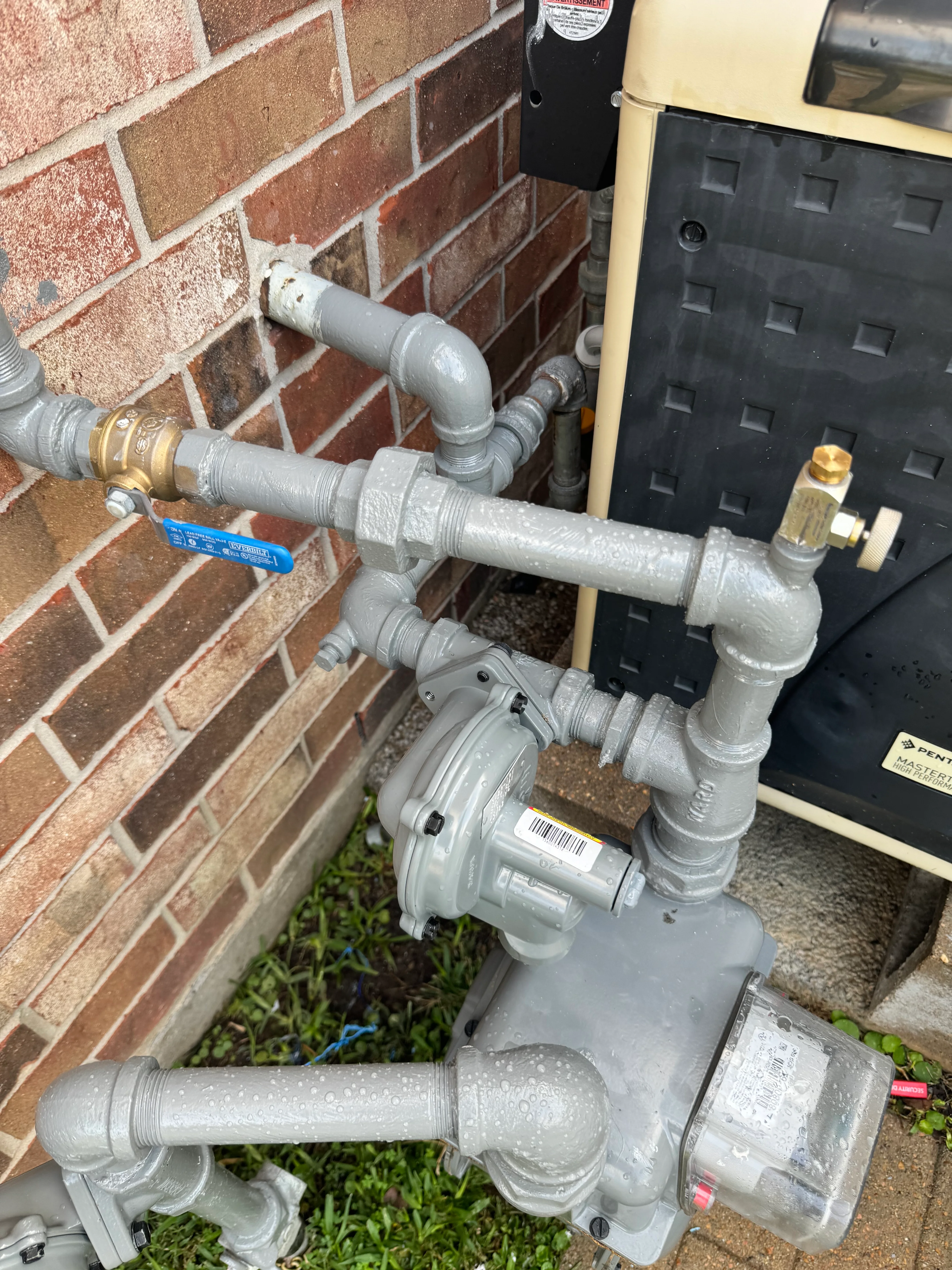 Gas meter installation with gray PVC piping and brass fittings on brick wall