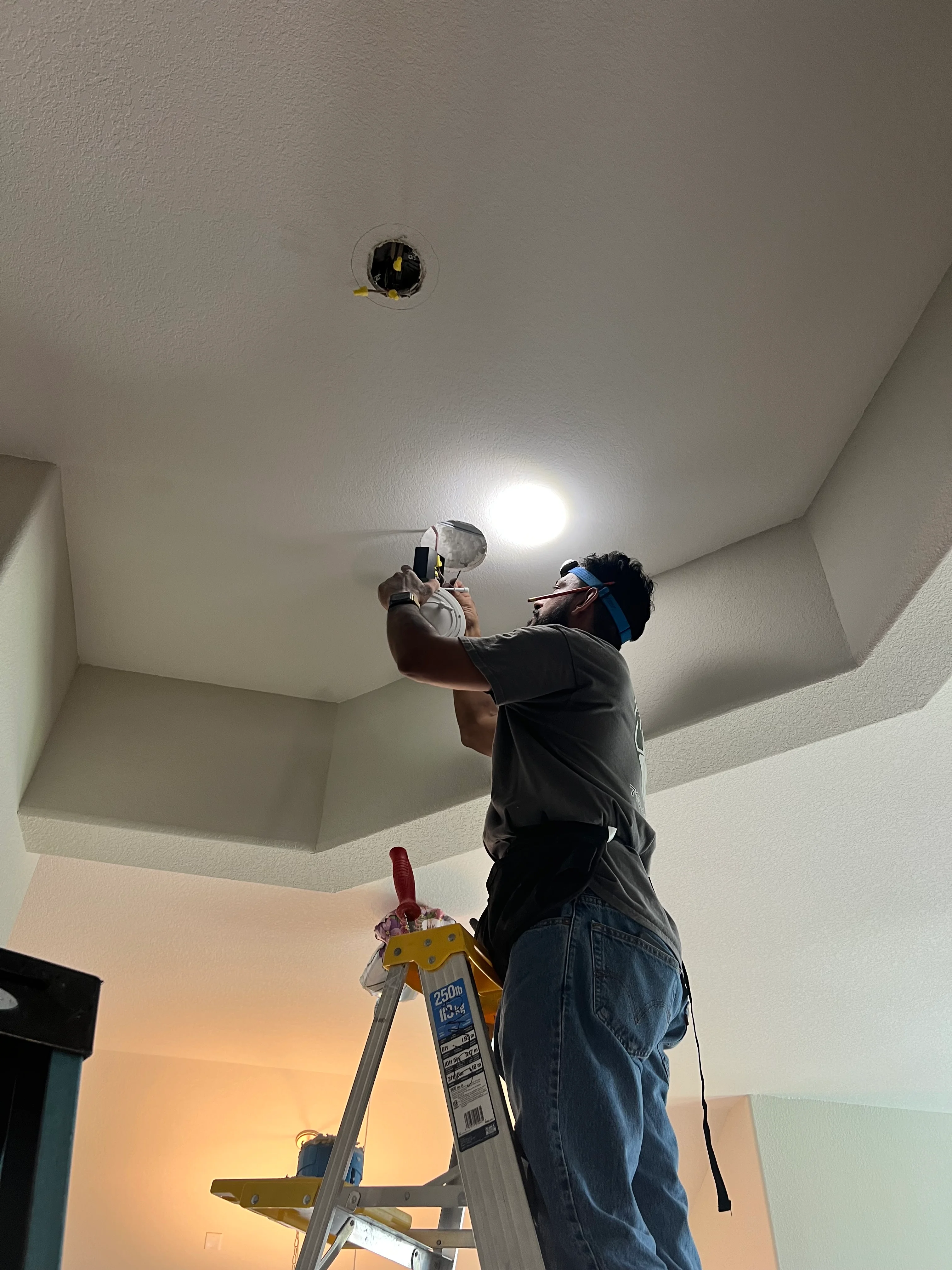 Electrician installing recessed ceiling light fixture in textured drywall ceiling