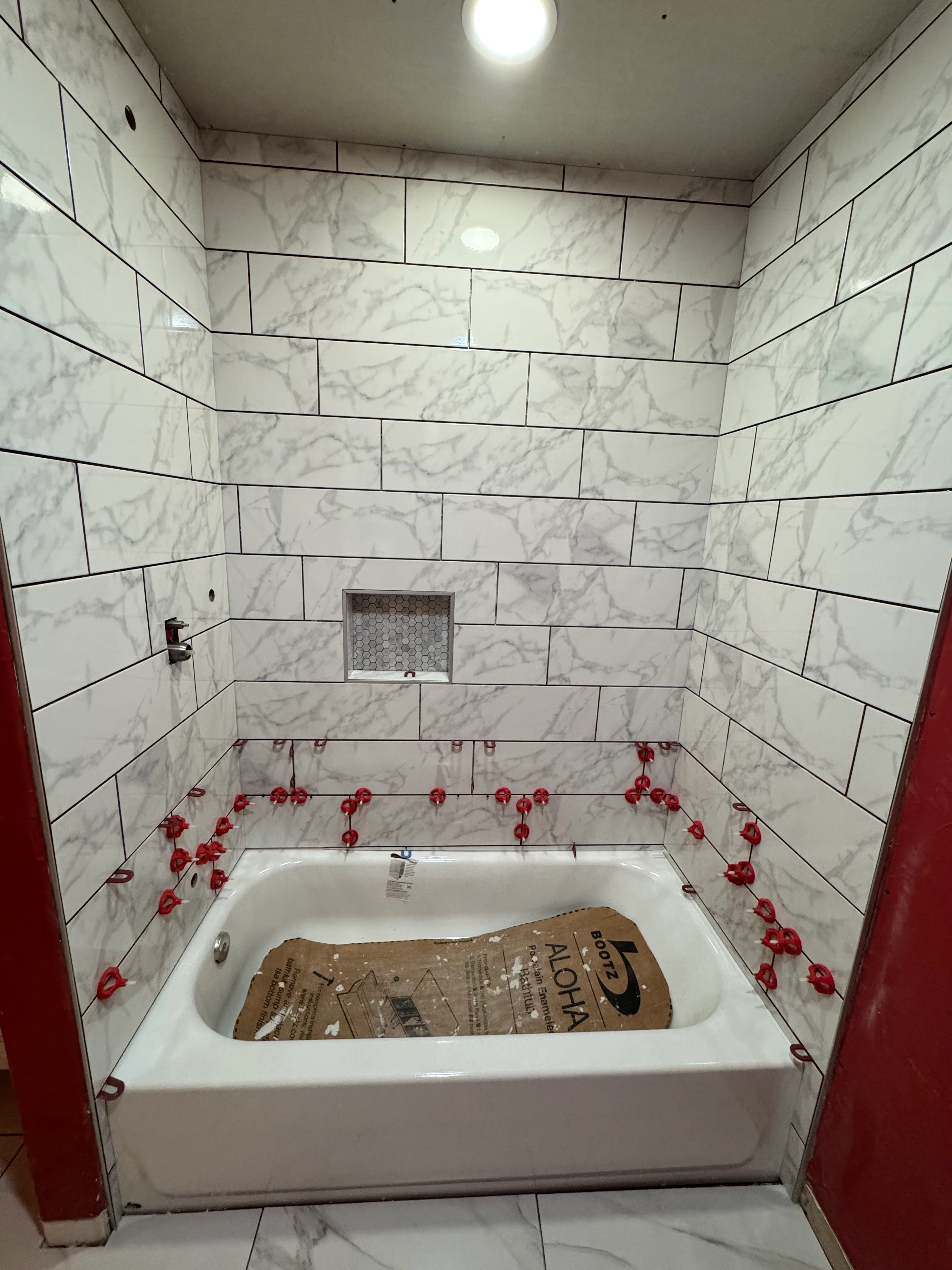 Newly tiled bathroom with white soaking tub and marble-look subway tile surround