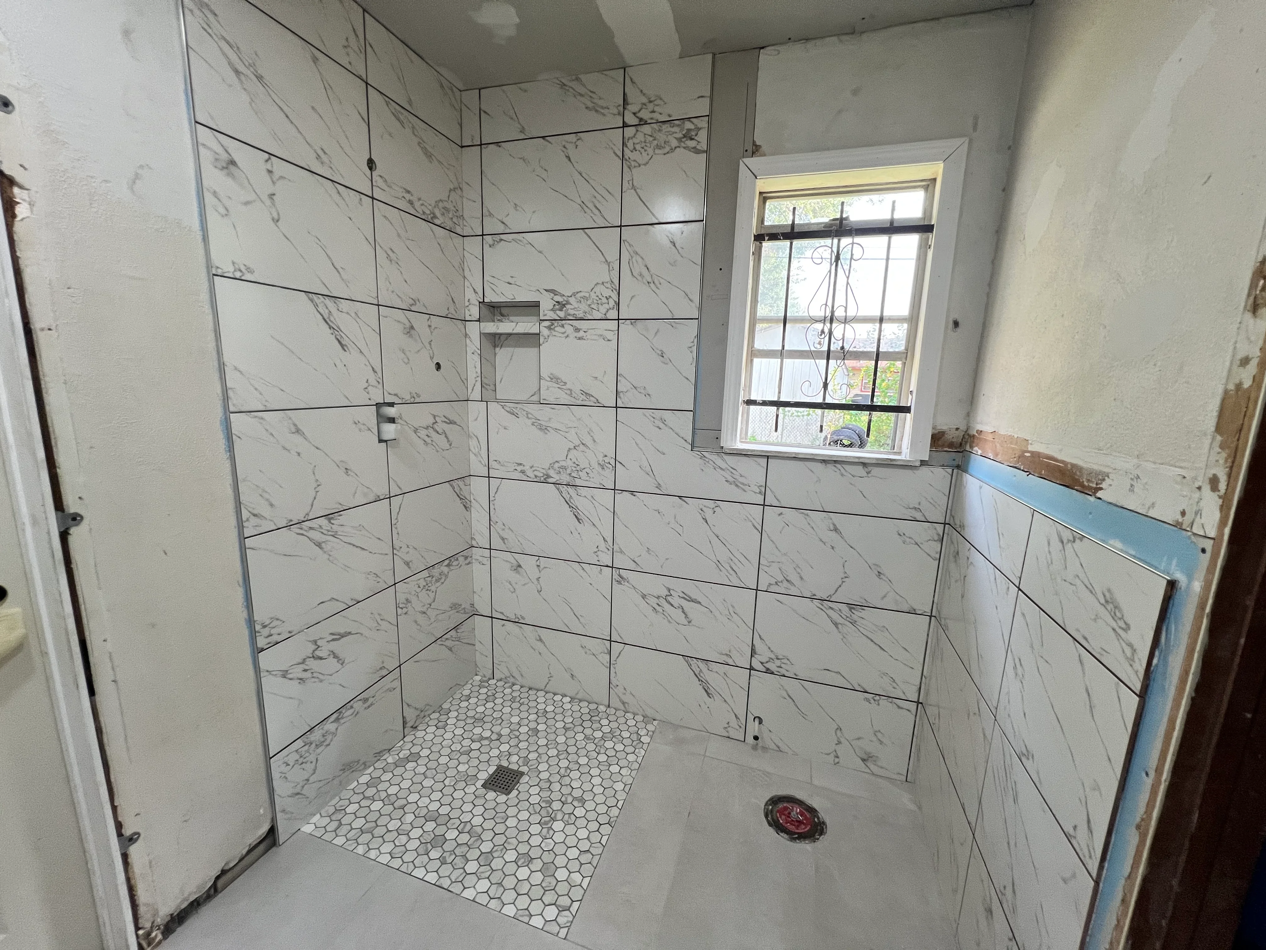 Walk-in shower with marble tile walls, hexagonal floor tiles, and frameless glass enclosure