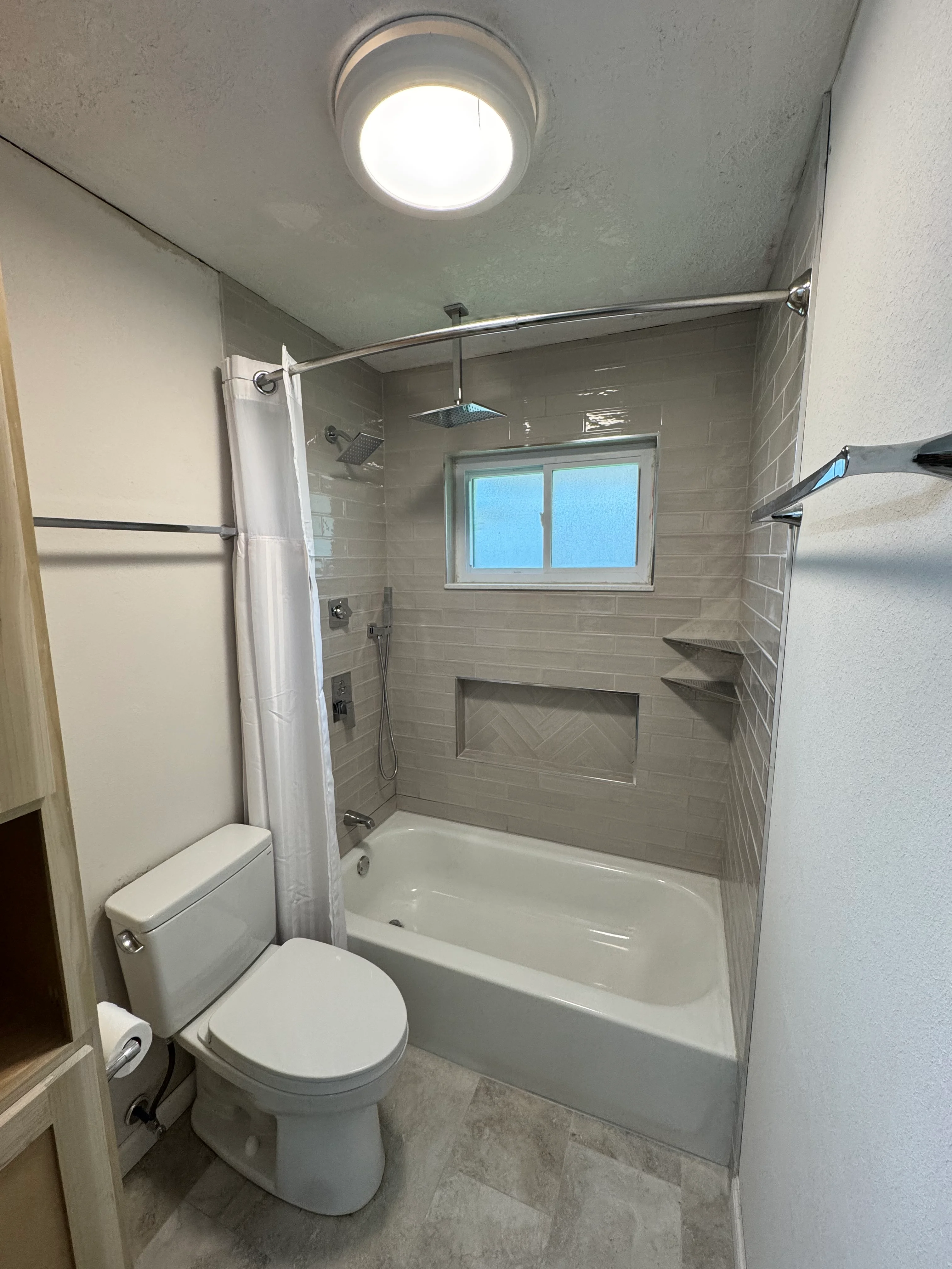 Modern bathroom with gray tile shower, glass enclosure, white toilet, and skylight