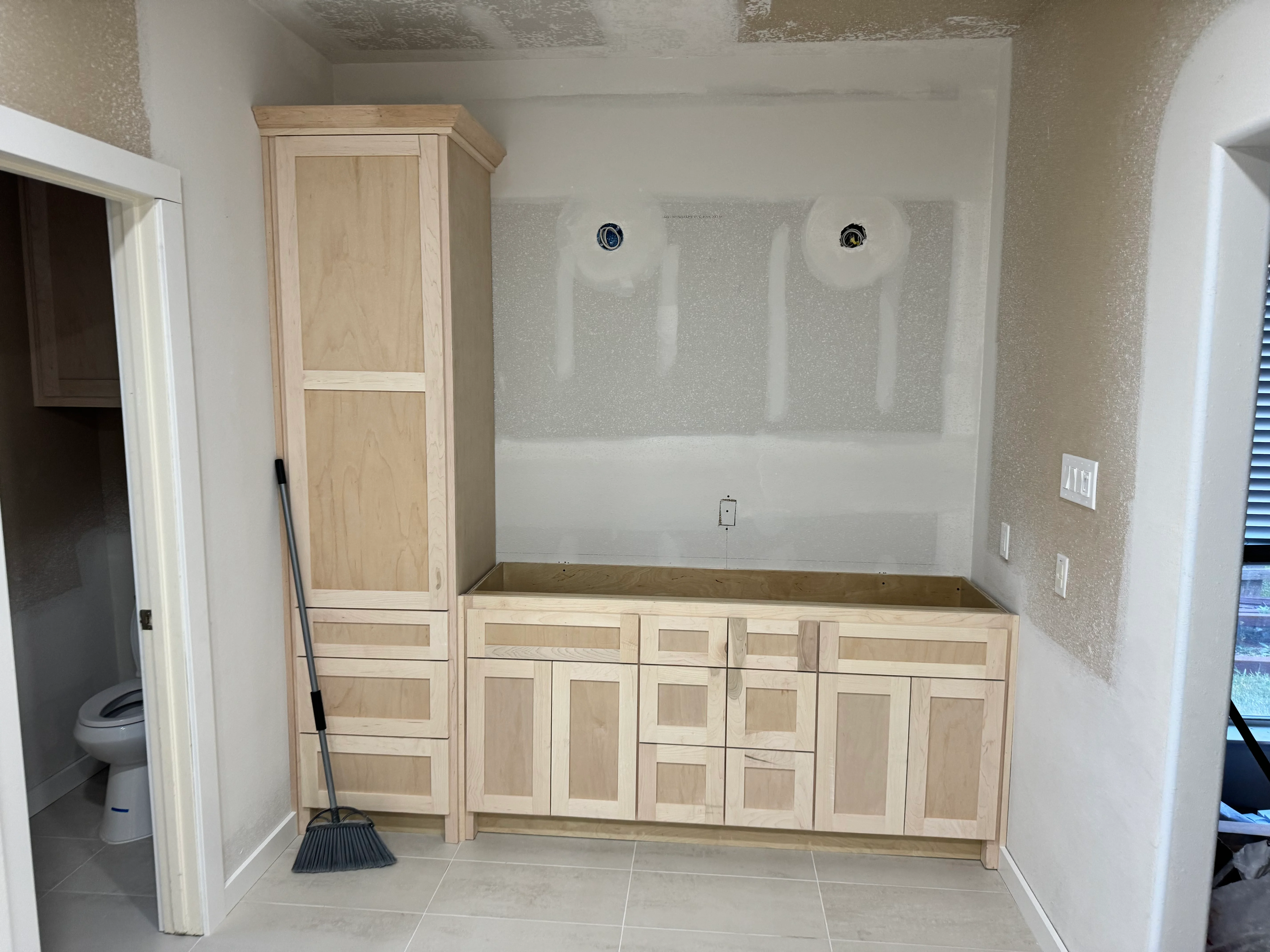Light wood bathroom vanity cabinets with dual sinks and tall linen tower in remodeled master bath