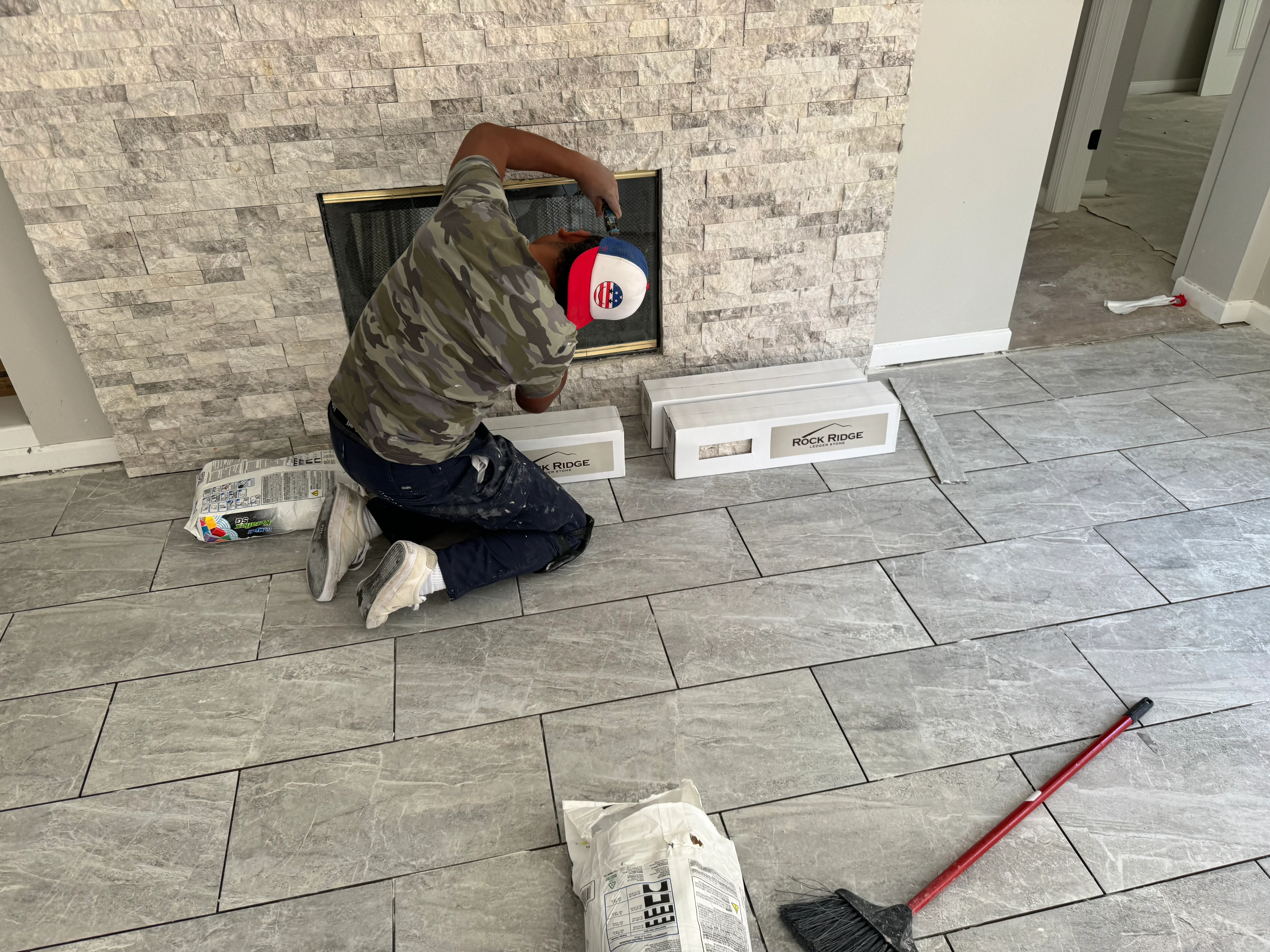 Worker installing stacked stone veneer around fireplace opening with new tile flooring