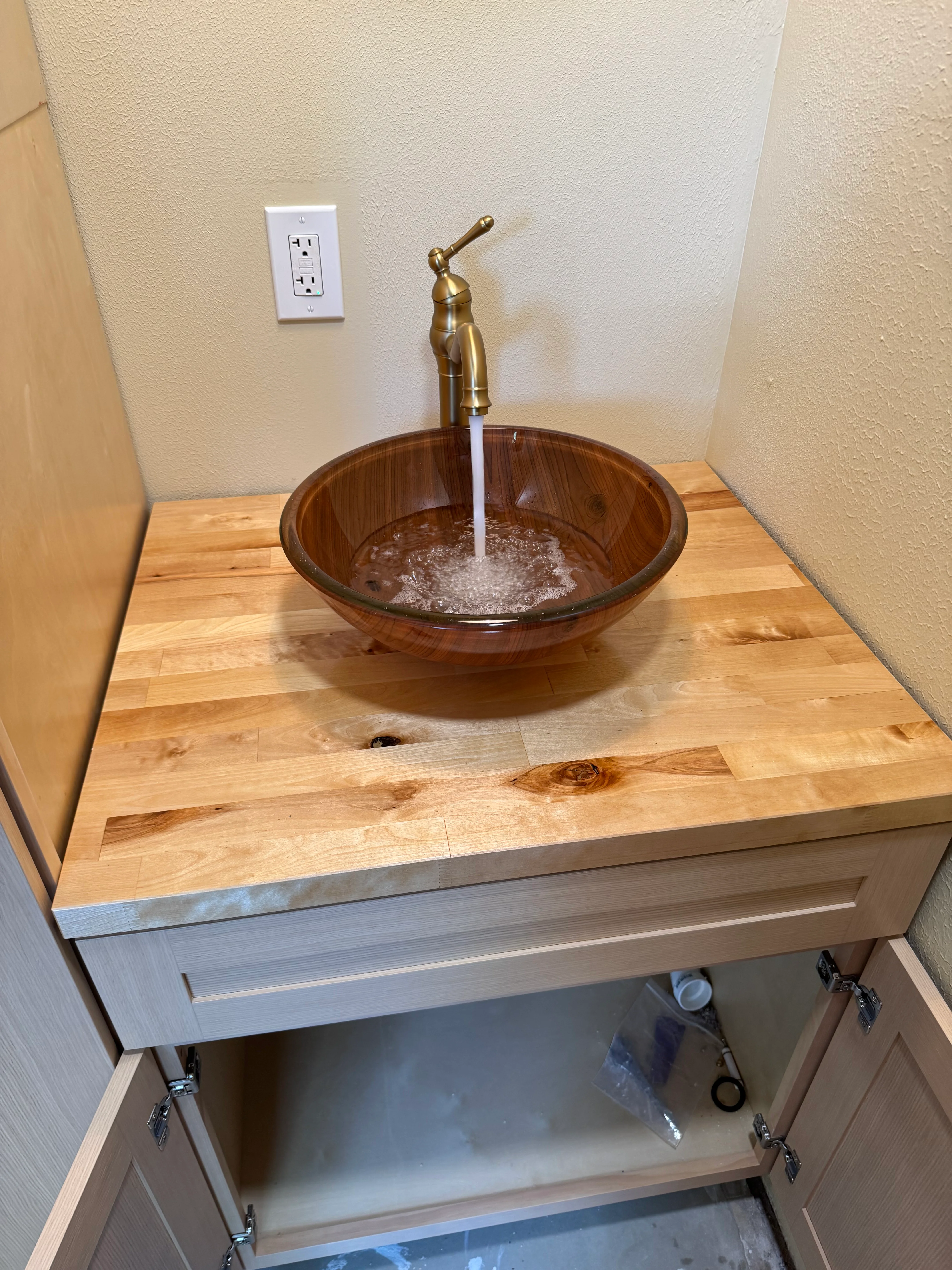 Wooden bathroom vanity with round glass vessel sink and brass faucet
