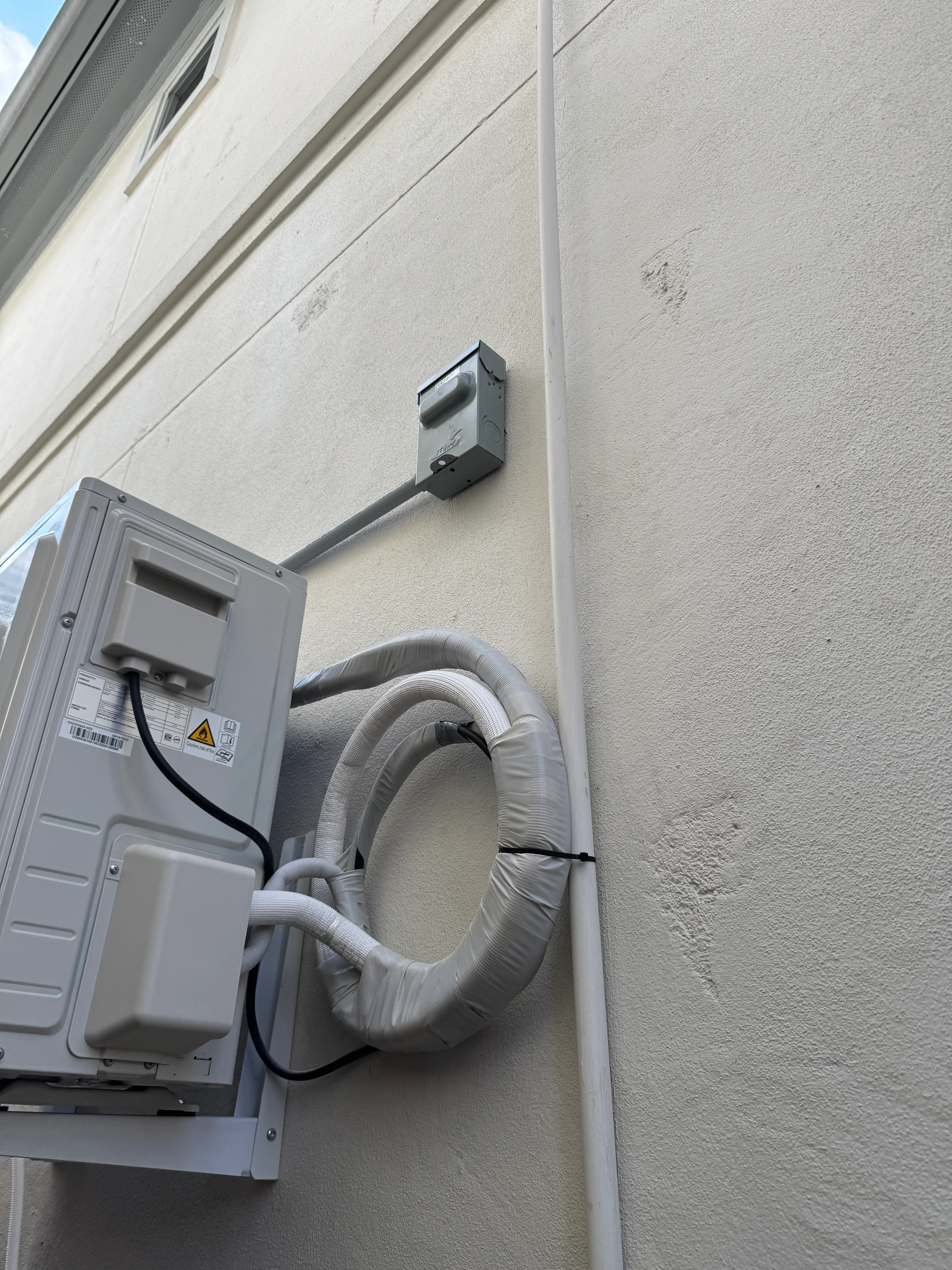 Exterior mini split HVAC unit with insulated white refrigerant lines mounted on stucco wall