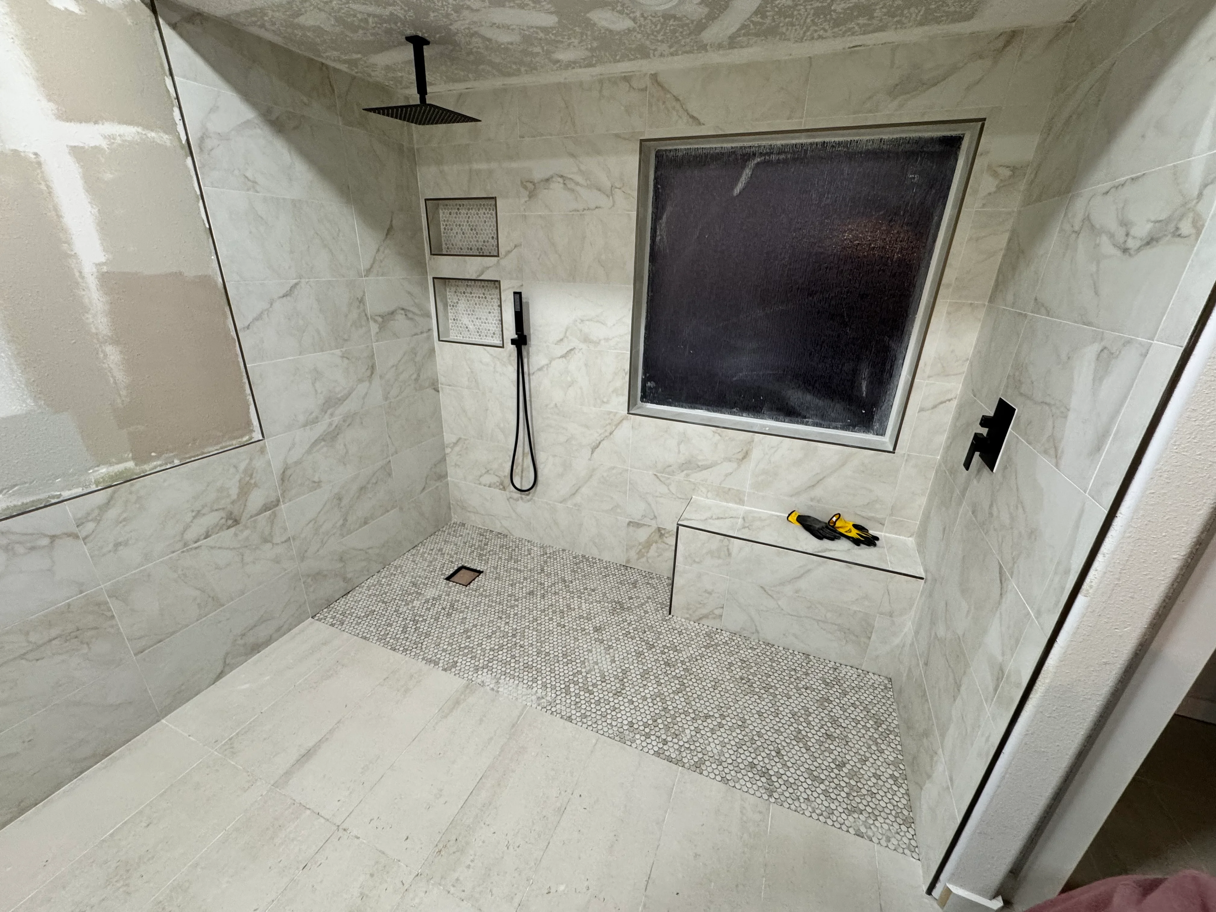 Modern bathroom shower with marble tile walls, mosaic floor, and frameless glass enclosure
