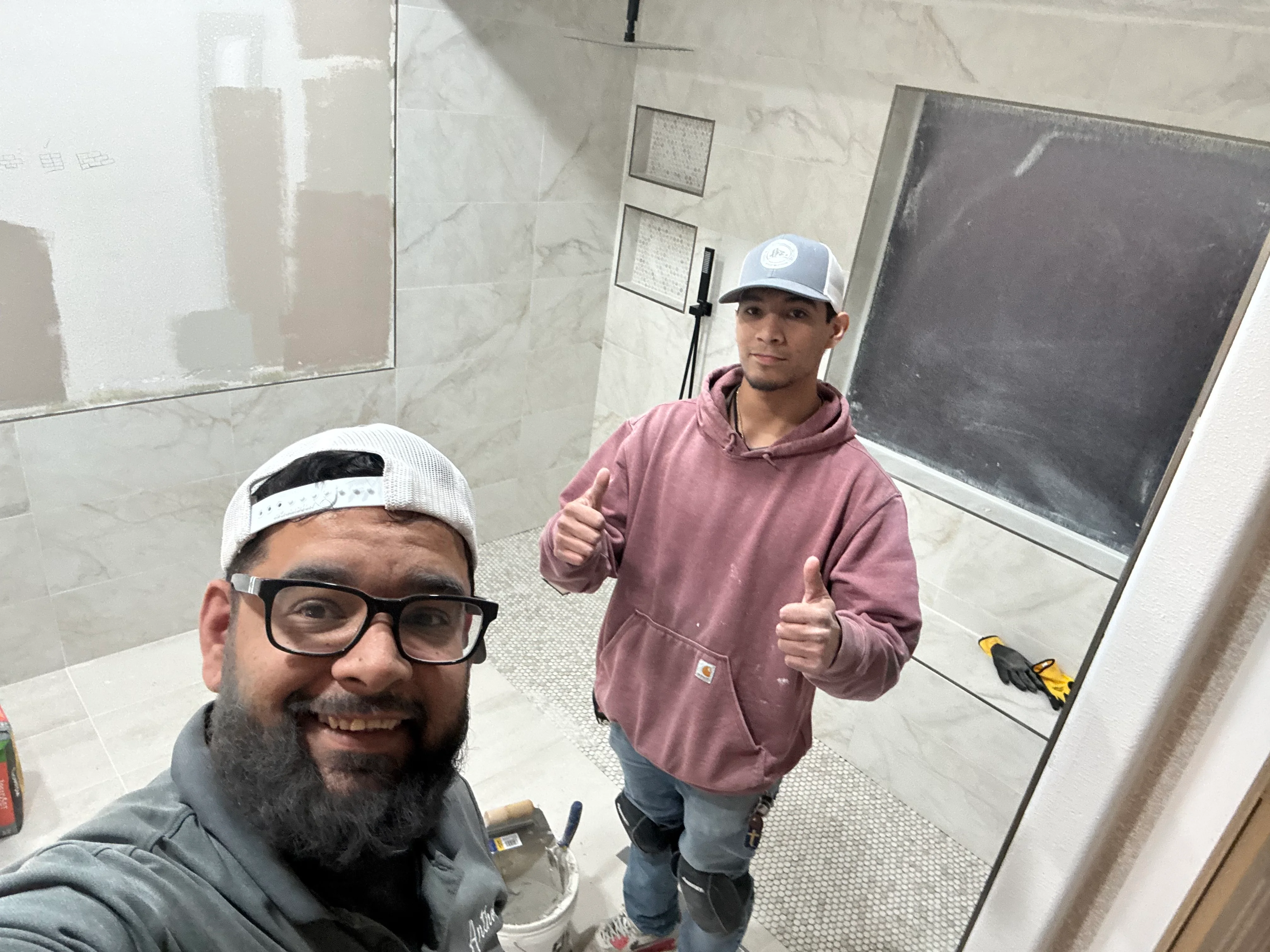 Two workers in bathroom with marble tile walls and frameless glass shower door installation