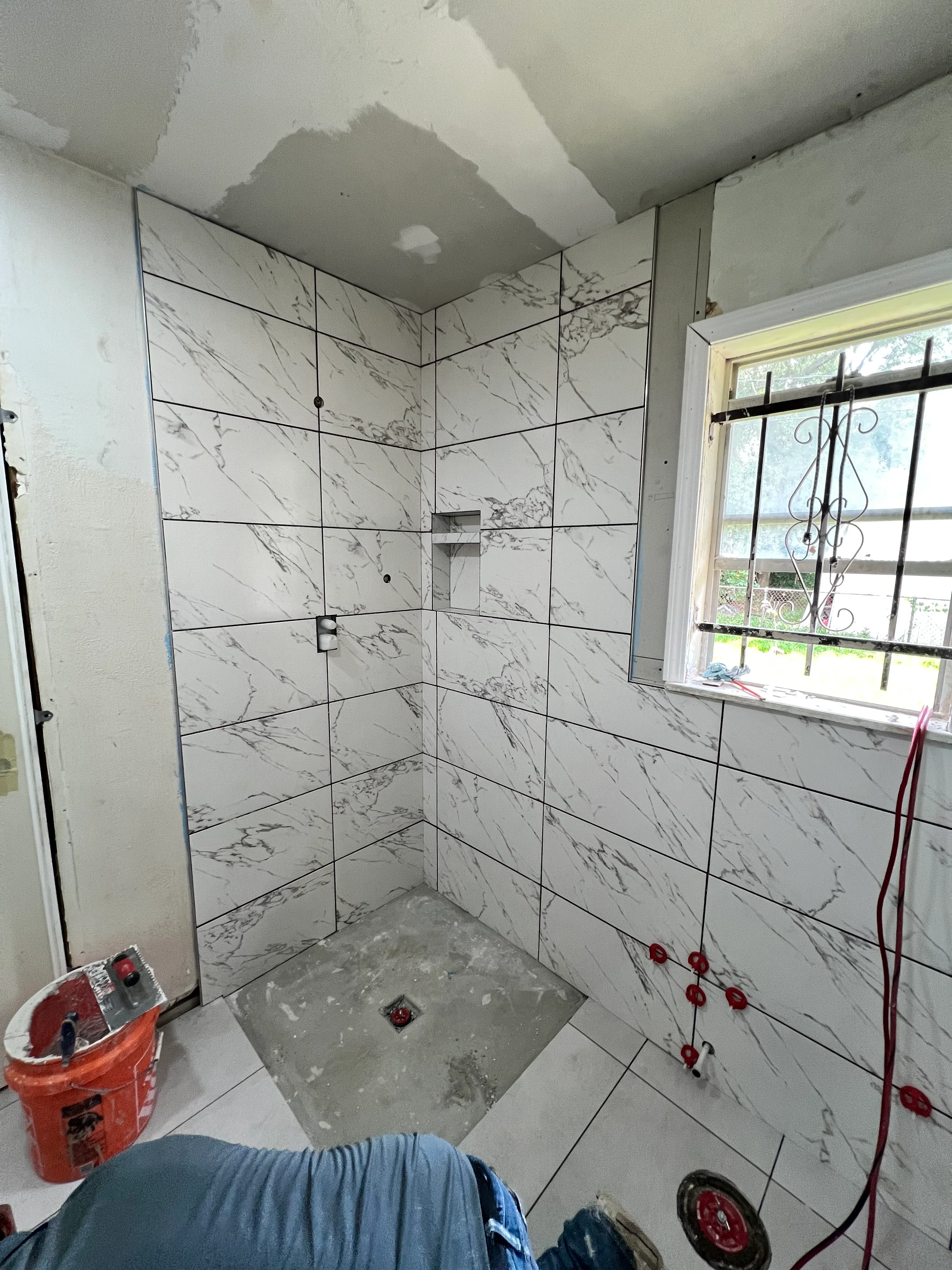 Newly tiled shower enclosure with marble-pattern porcelain tiles and frameless glass doors
