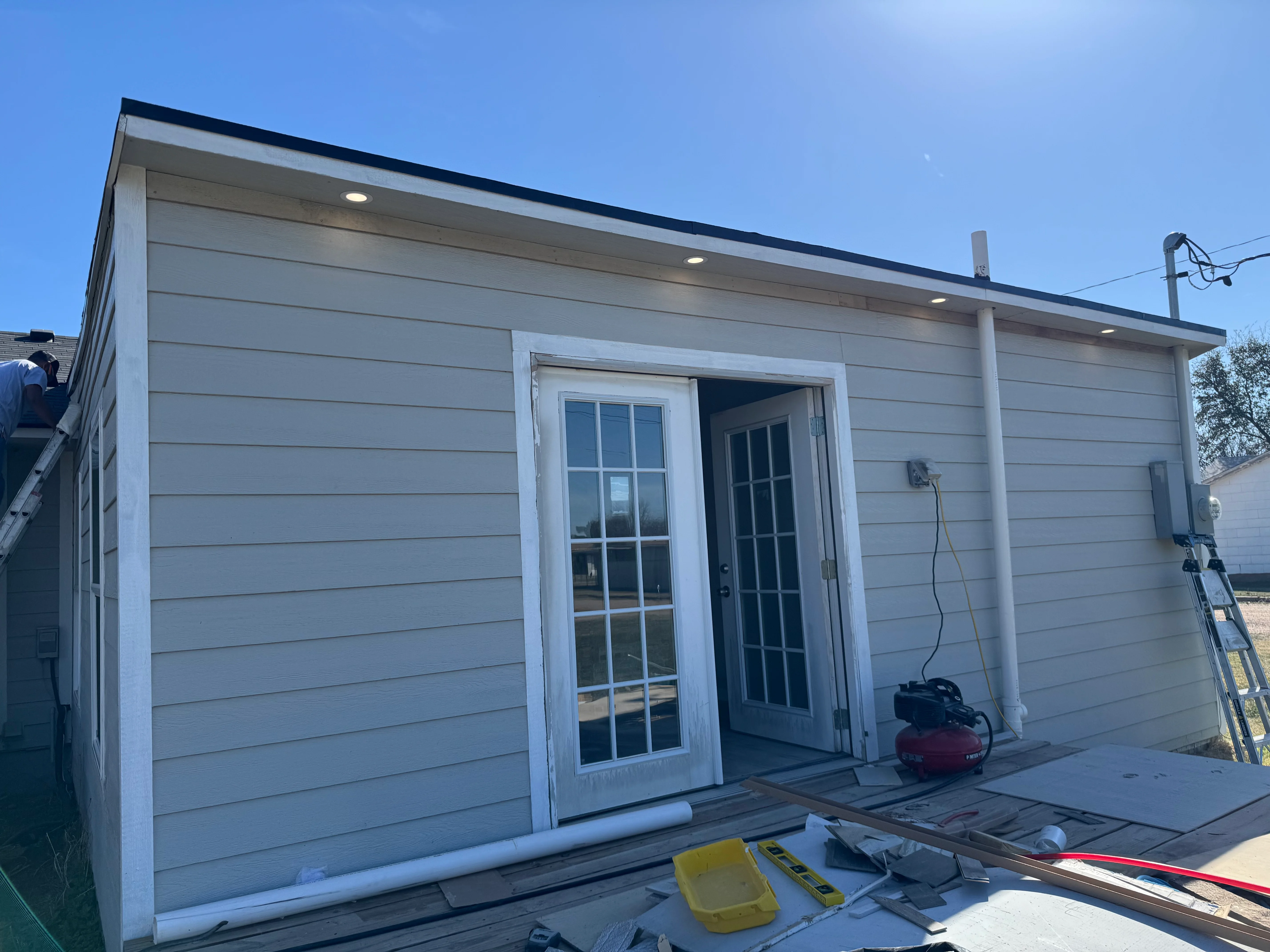 Modern gray composite siding ADU with glass doors and recessed lighting under construction