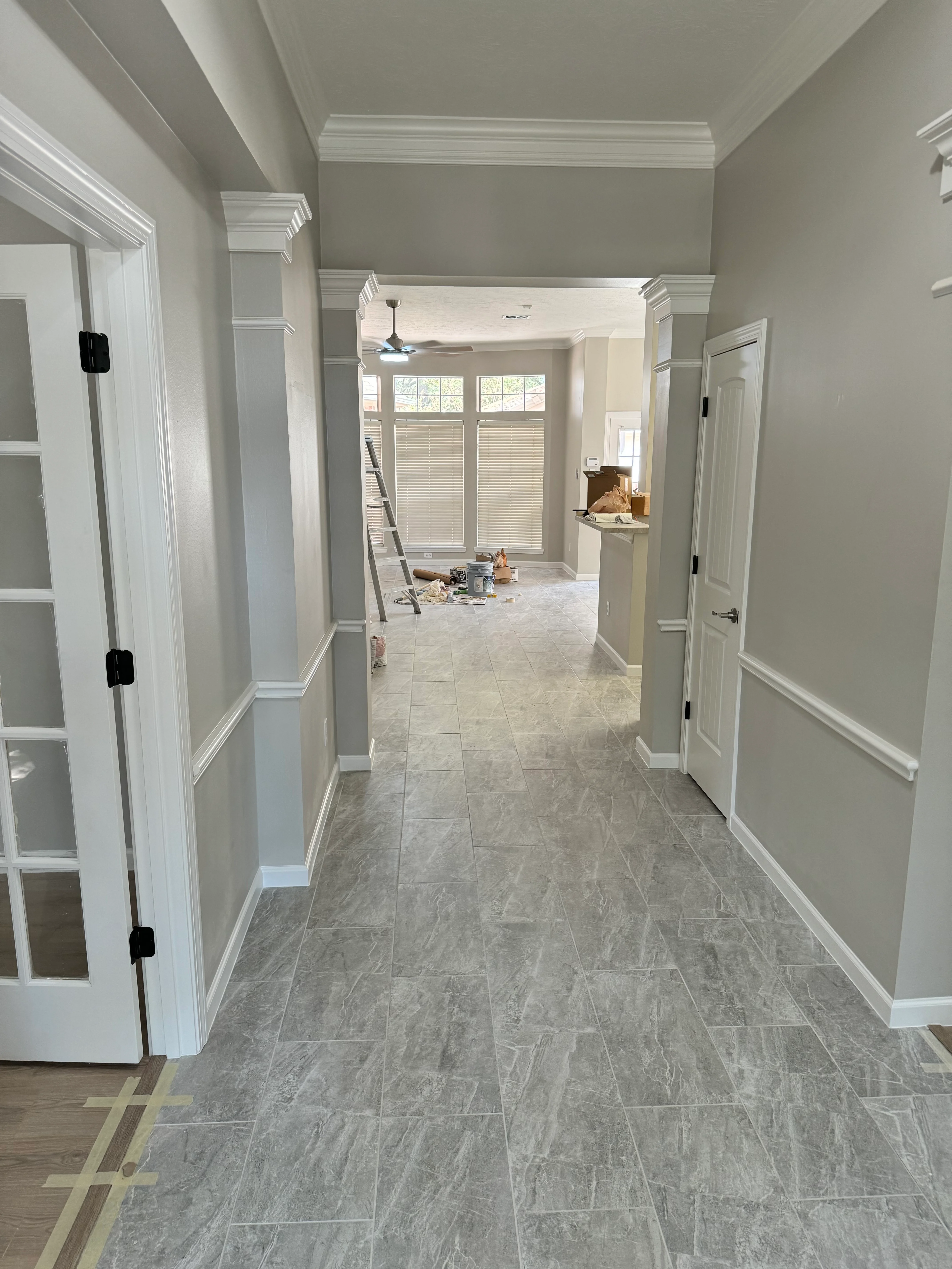 Modern hallway with gray tile flooring, white trim, and multiple doorways leading to renovated bathroom space