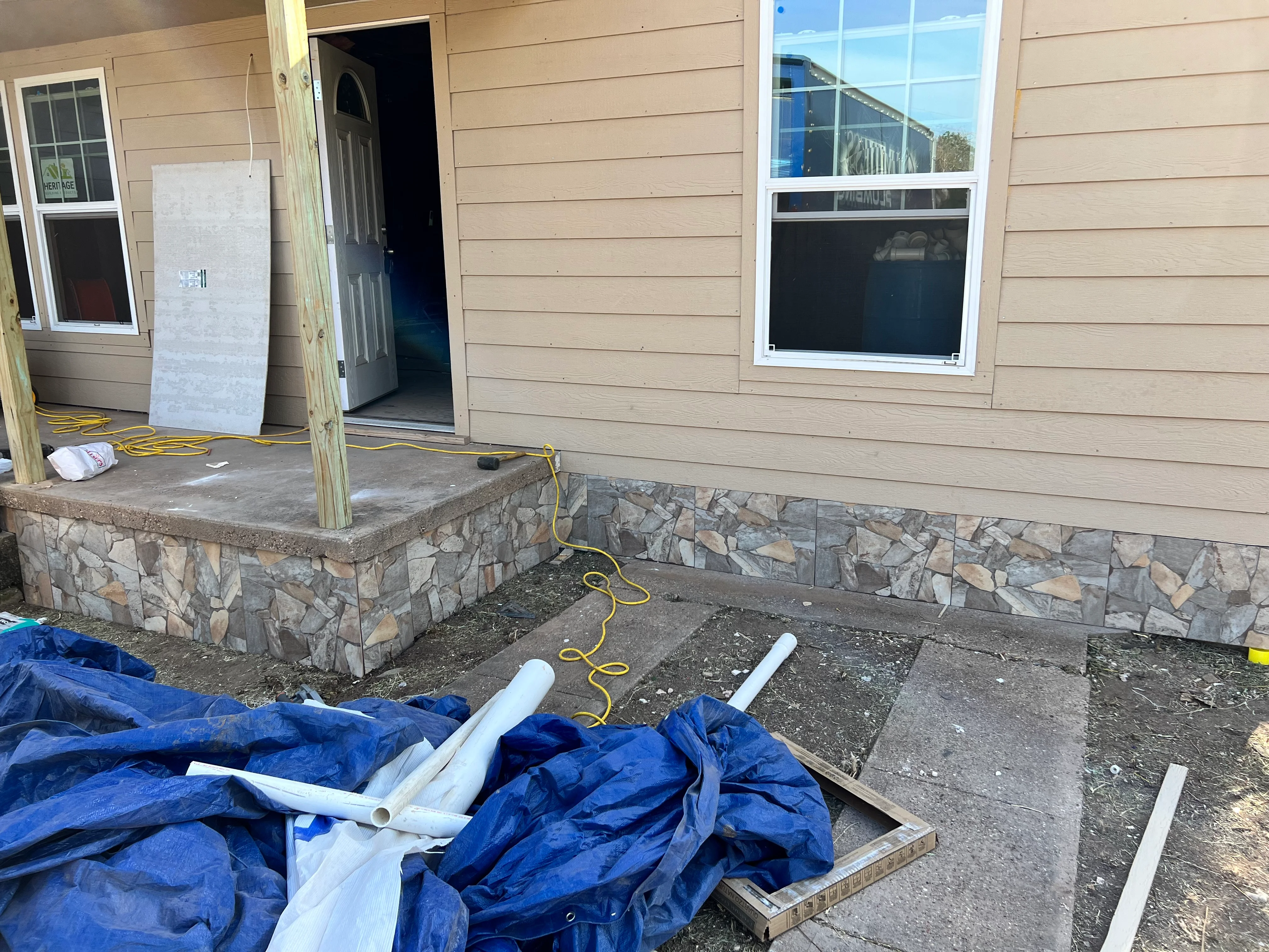 Stone veneer foundation with concrete porch during active renovation with protective coverings