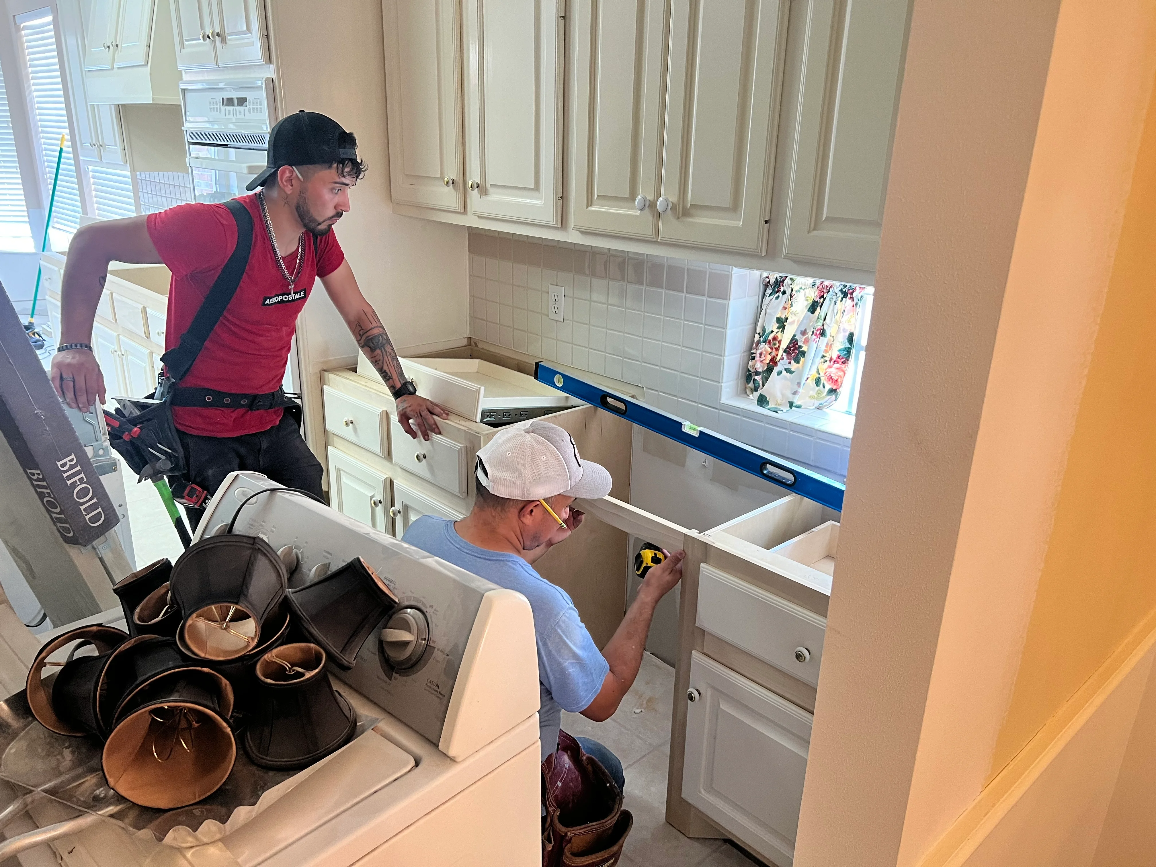 Two workers installing white kitchen cabinets and measuring countertop during remodel