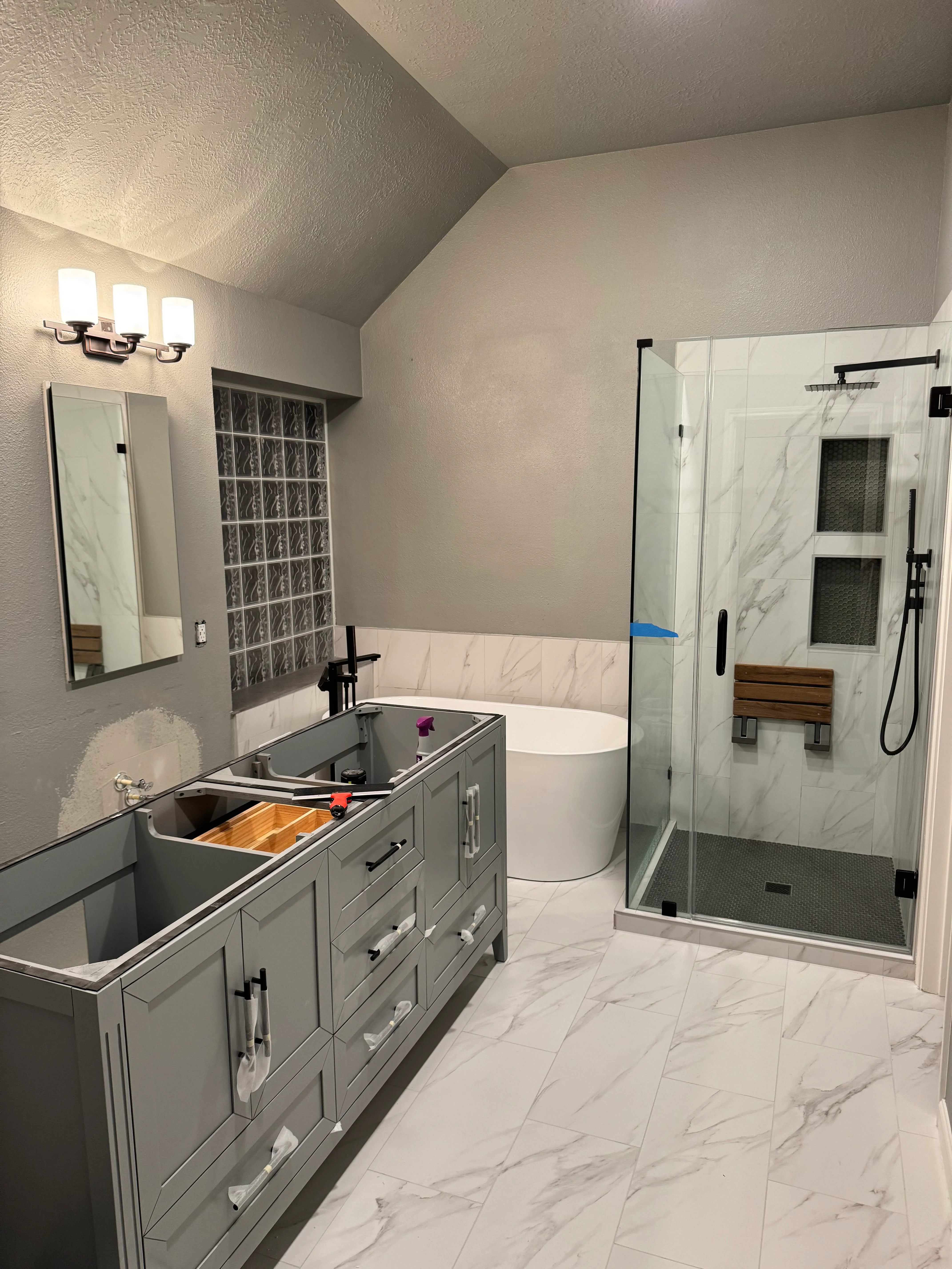 Modern master bathroom with marble tile, gray vanity, and frameless glass shower enclosure