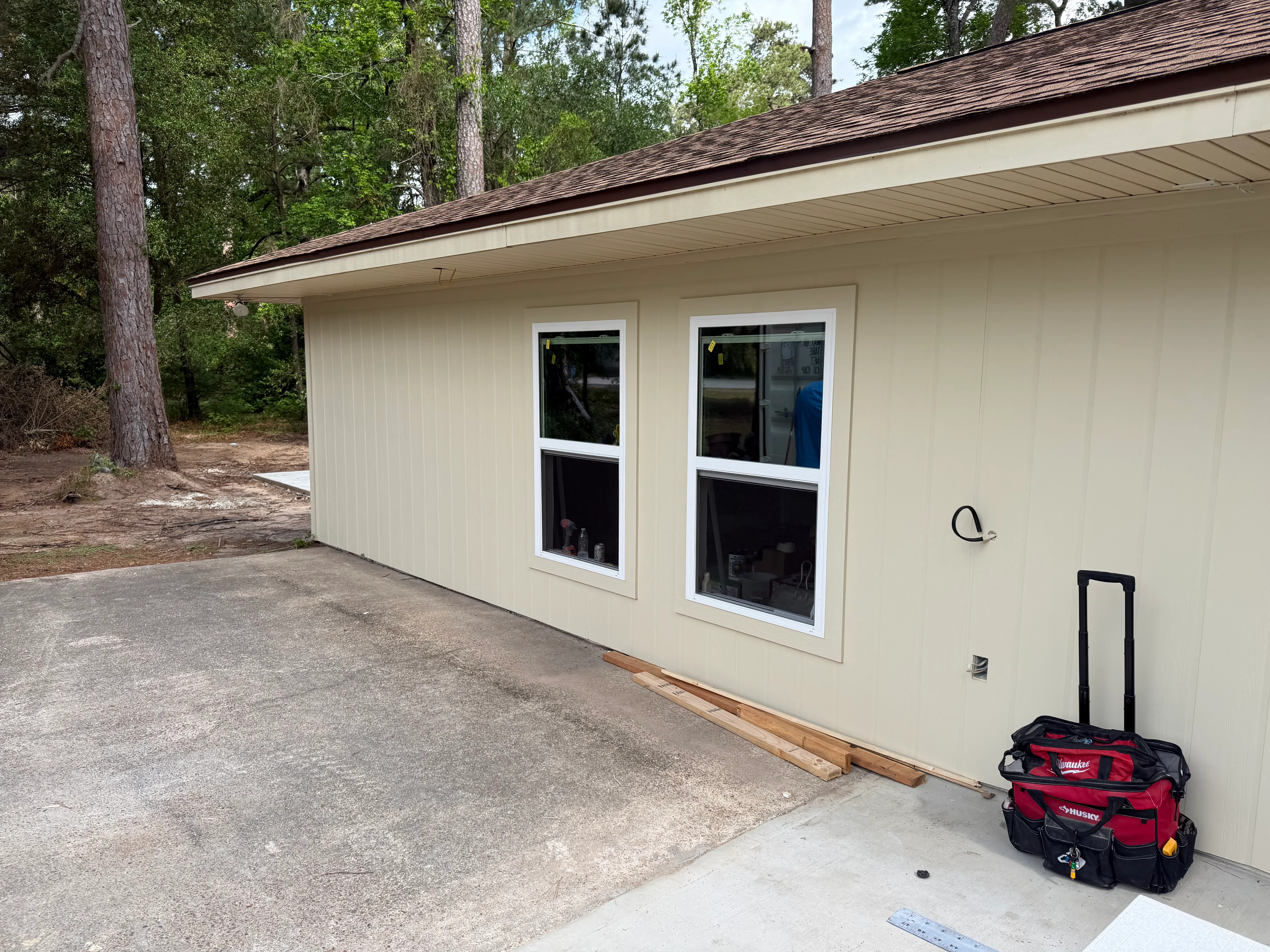 Cream-colored carport addition with dark roof and aluminum windows in wooded setting