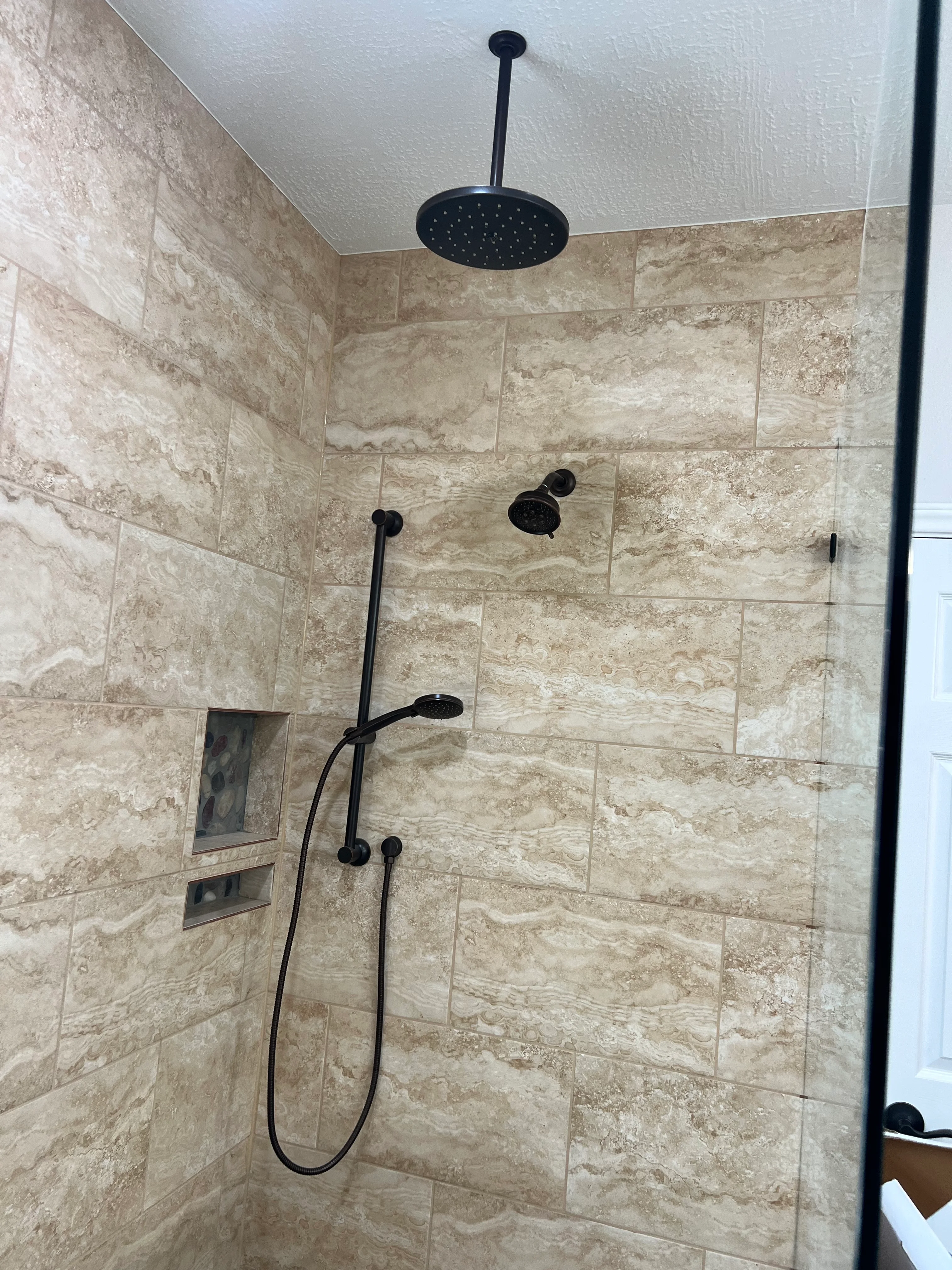 Luxury shower with travertine tile walls, black rainfall showerhead, and dual body jets